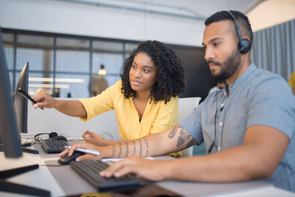 Two agents in headsets at a workstation, one pointing out detail on the screen