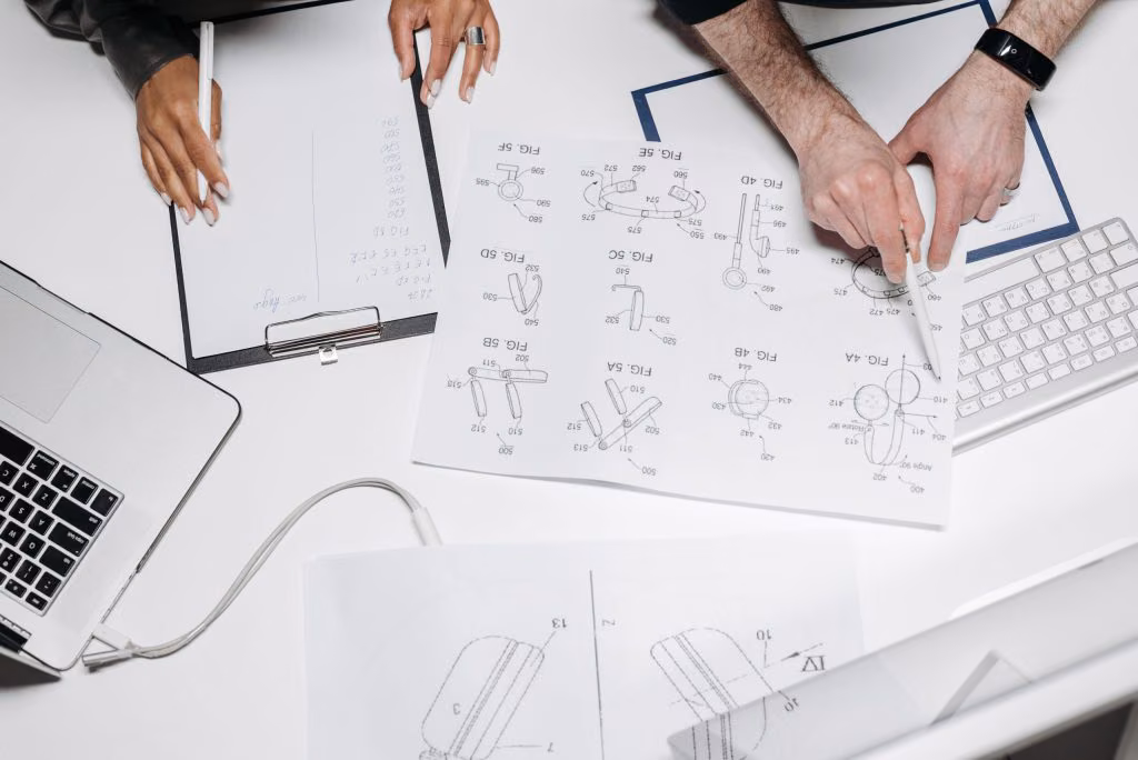 Two people reviewing technical drawings beside a laptop and keyboard
