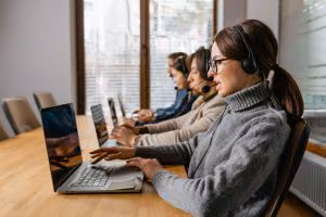 Row of contact centre agents in headsets working at laptops in an open-plan office
