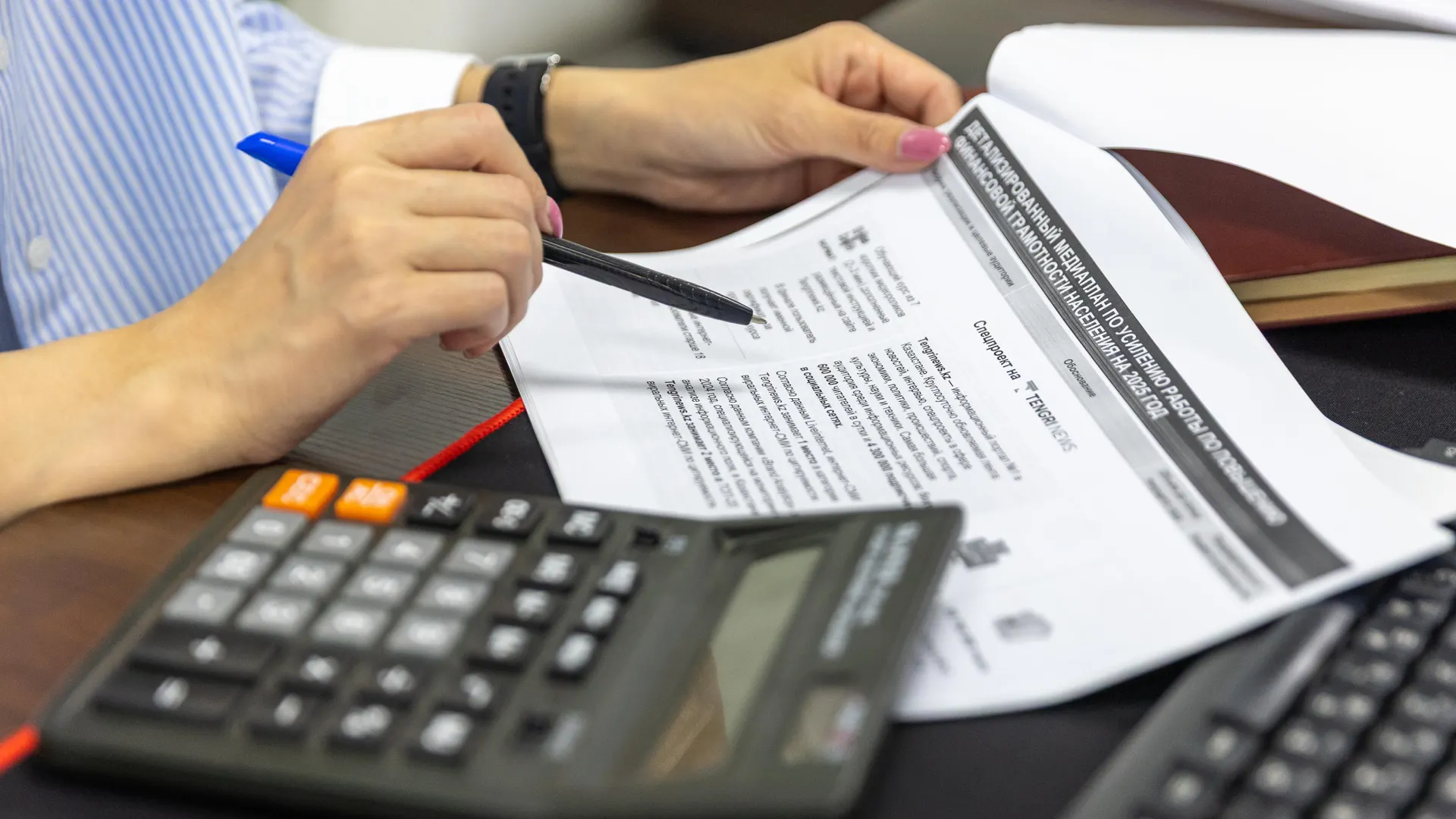 Close-up of a person analyzing financial documents using a calculator and pen