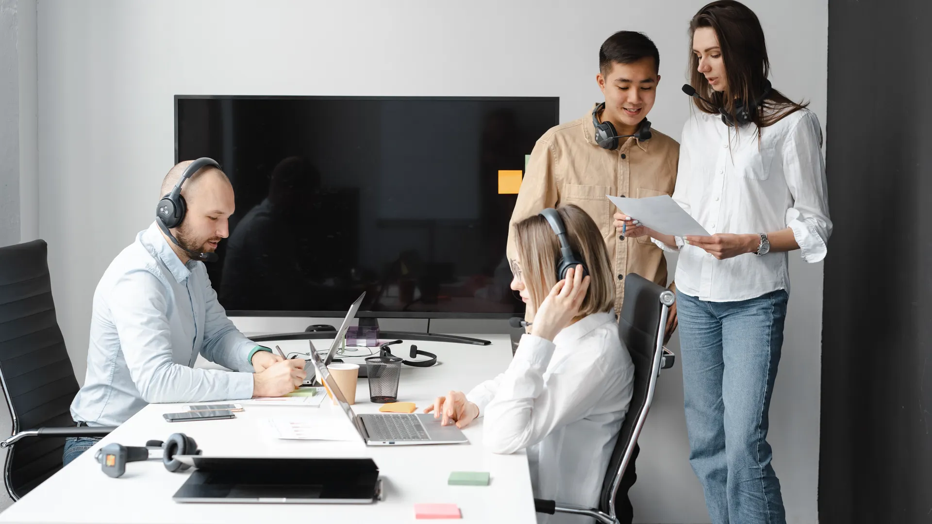 A diverse group of coworkers collaborating in a modern office space with headsets and laptops