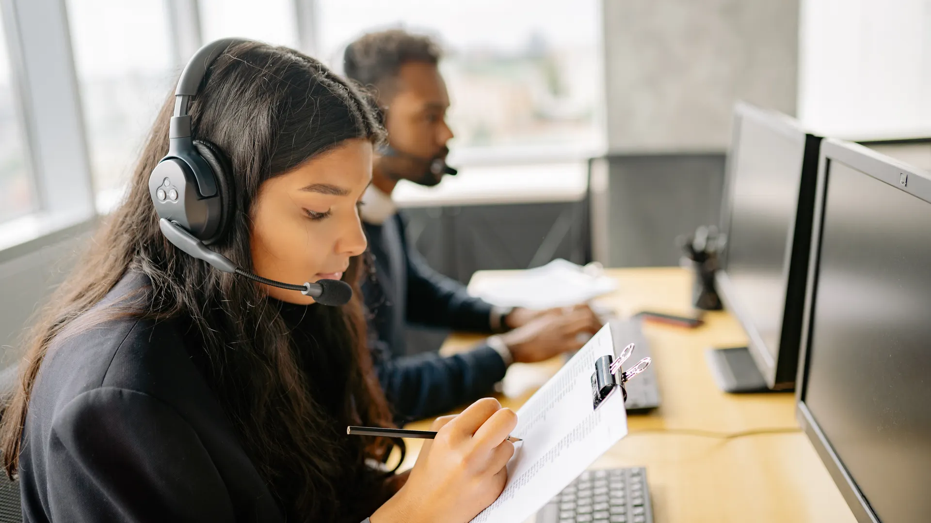 Two call center agents wearing headsets working at desks with computers in a modern office