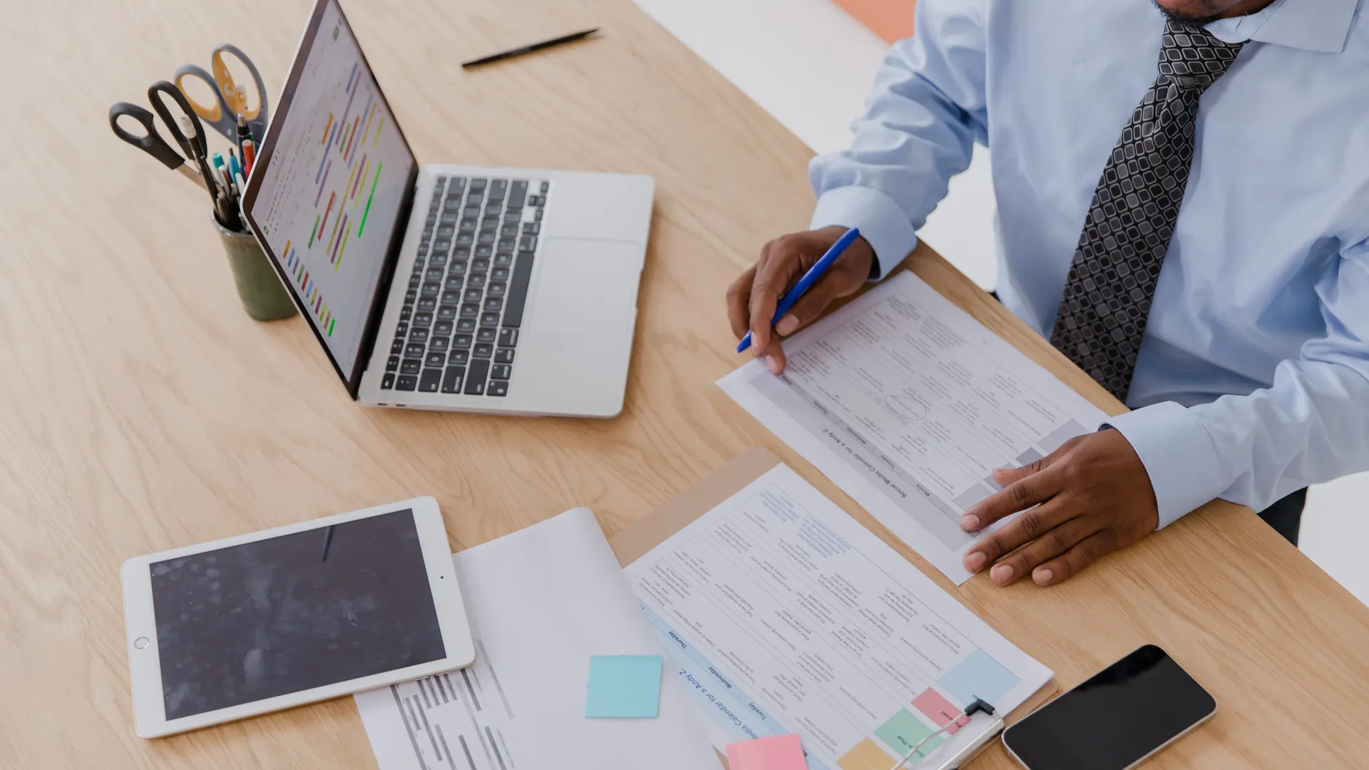 High angle view of a businessman working at a desk with a laptop, tablet, and documents