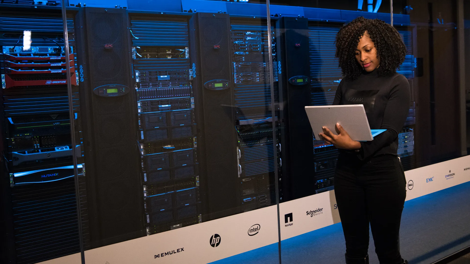 A female engineer using a laptop while monitoring data servers in a modern server room