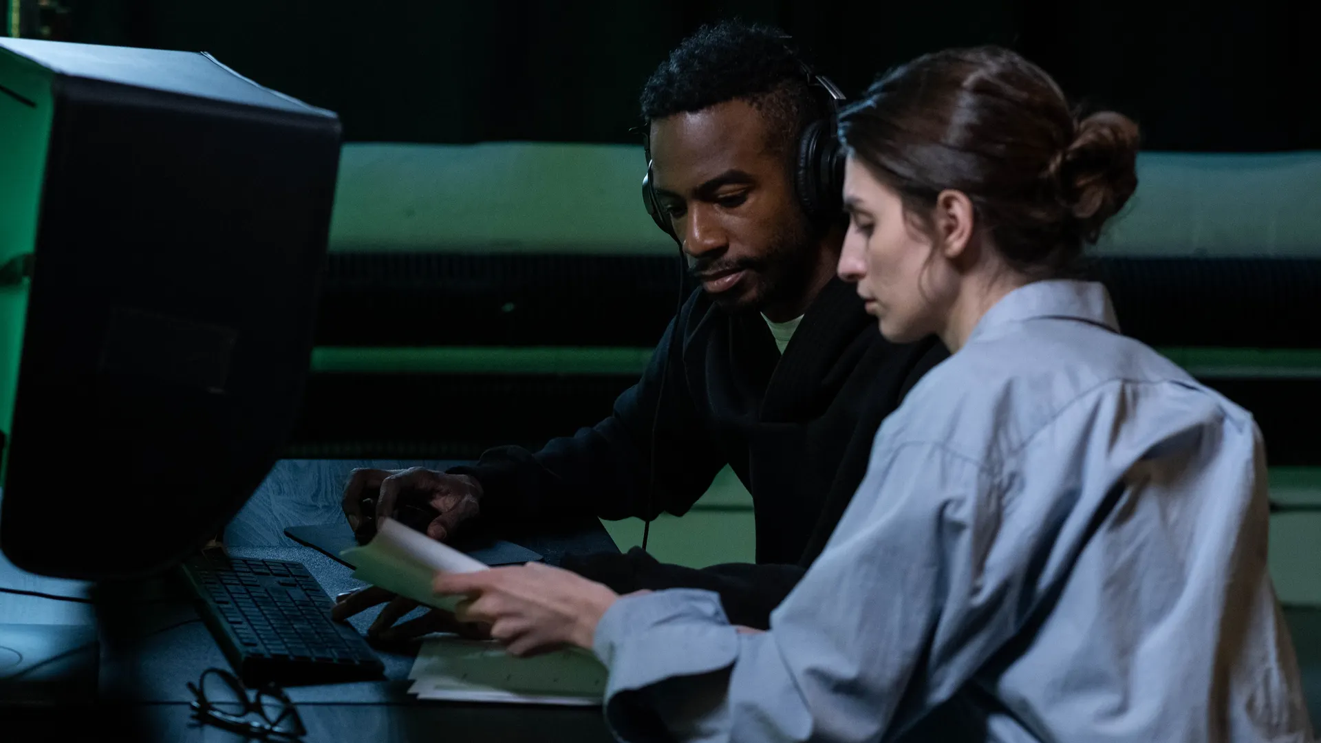Two colleagues engaged in focused editing work at a computer, collaborating effectively
