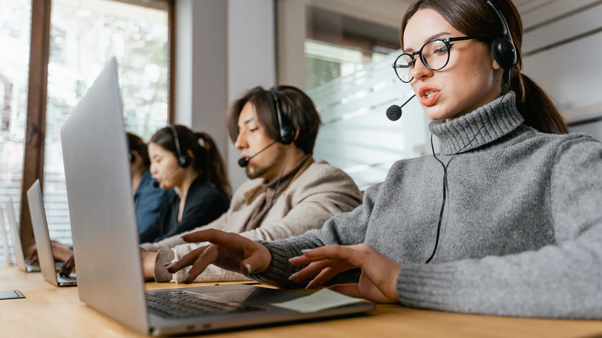 Four call center employees working with headsets and laptops in a modern office setting
