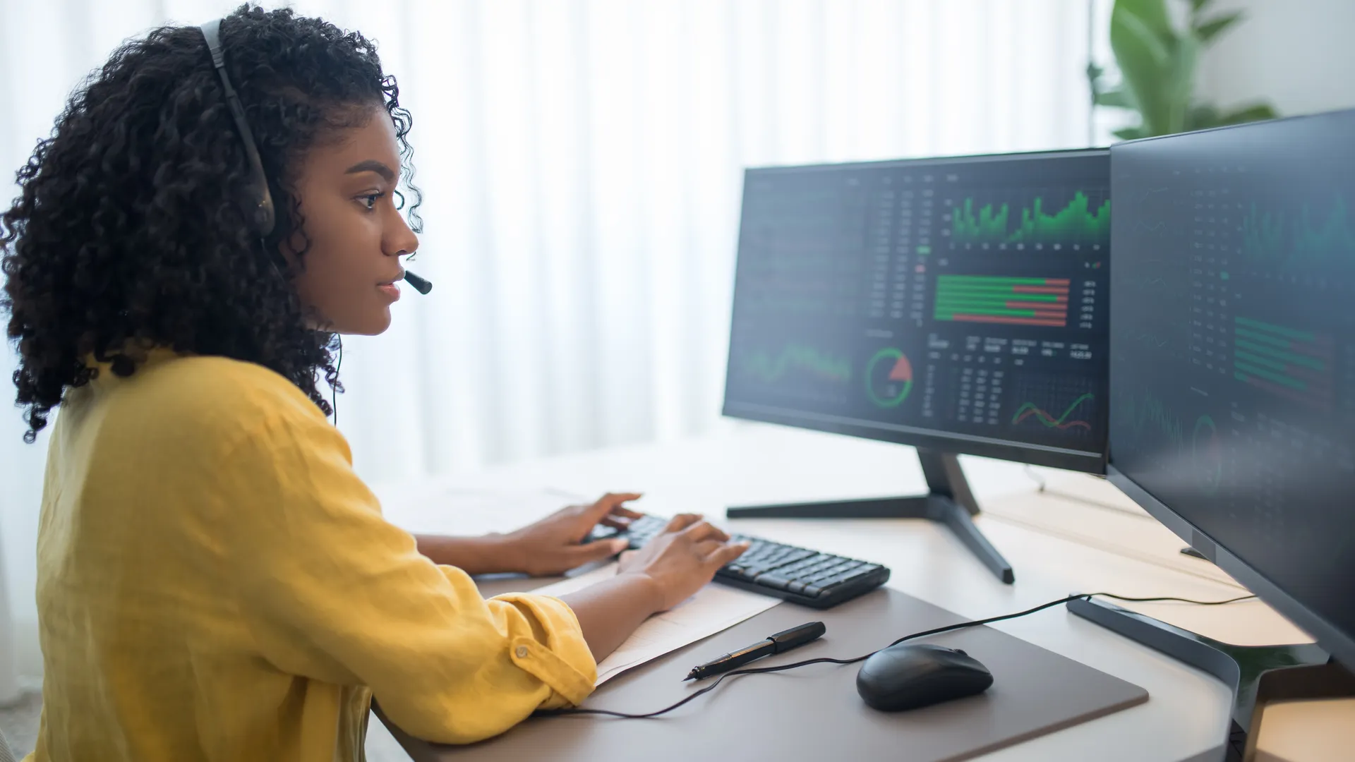 African American woman working in office analyzing data on dual computer monitors
