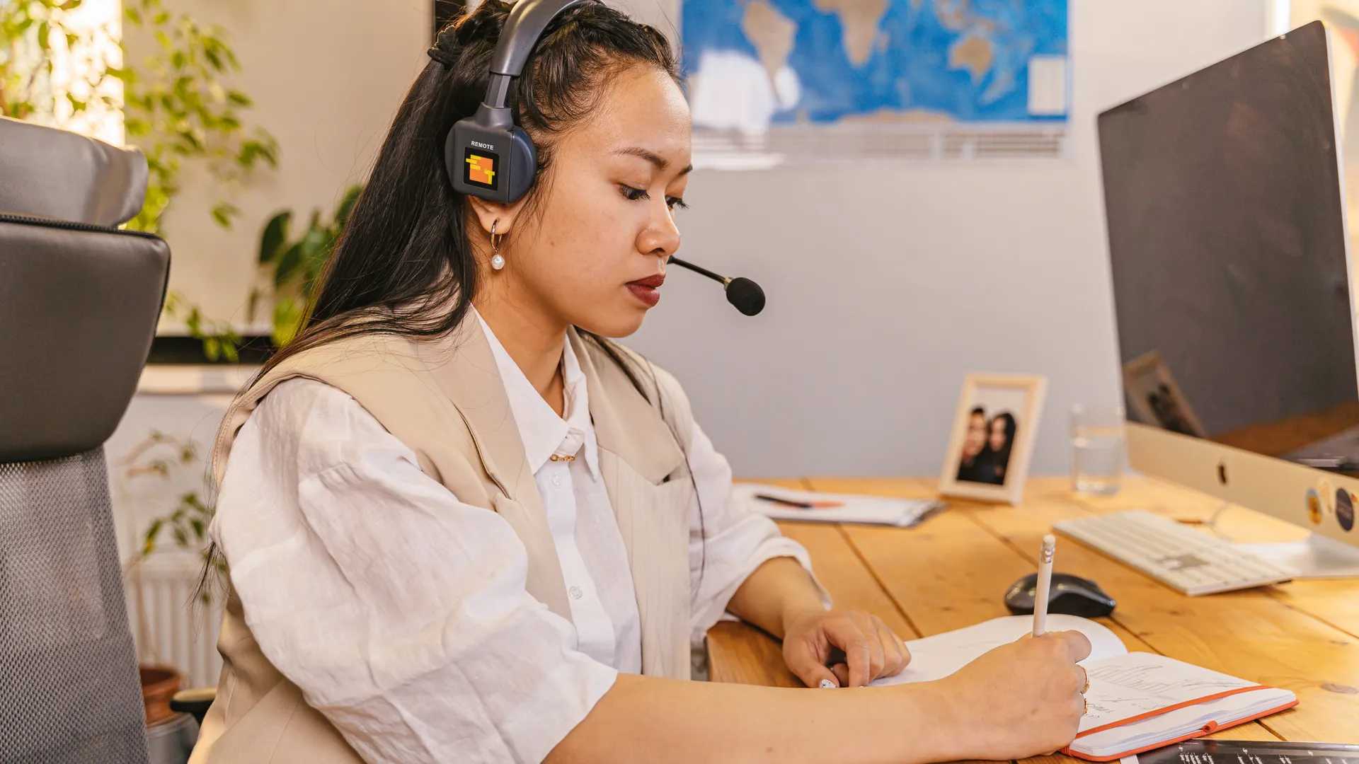 Businesswoman in an office environment wearing a headset and writing notes