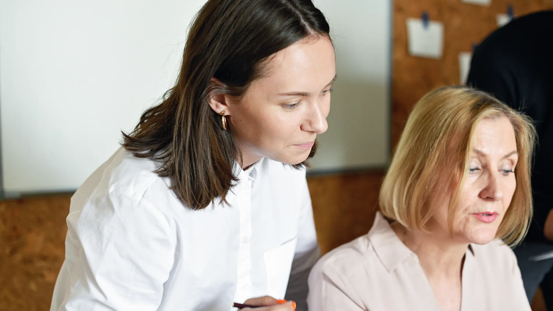 Two professional women discussing work collaboratively in a modern office environment