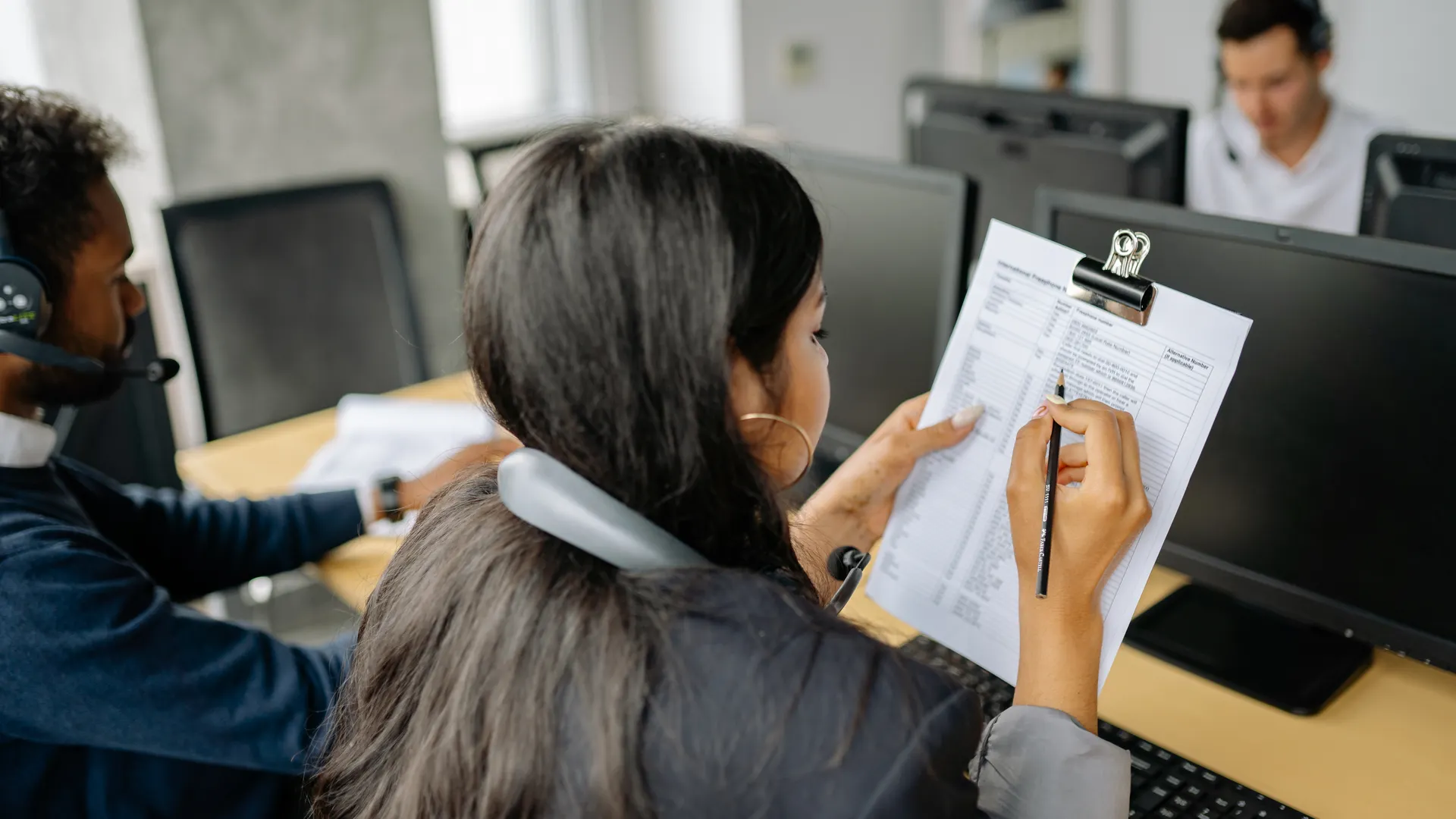 Focused call center employee reviewing documents while on a call in an office setting