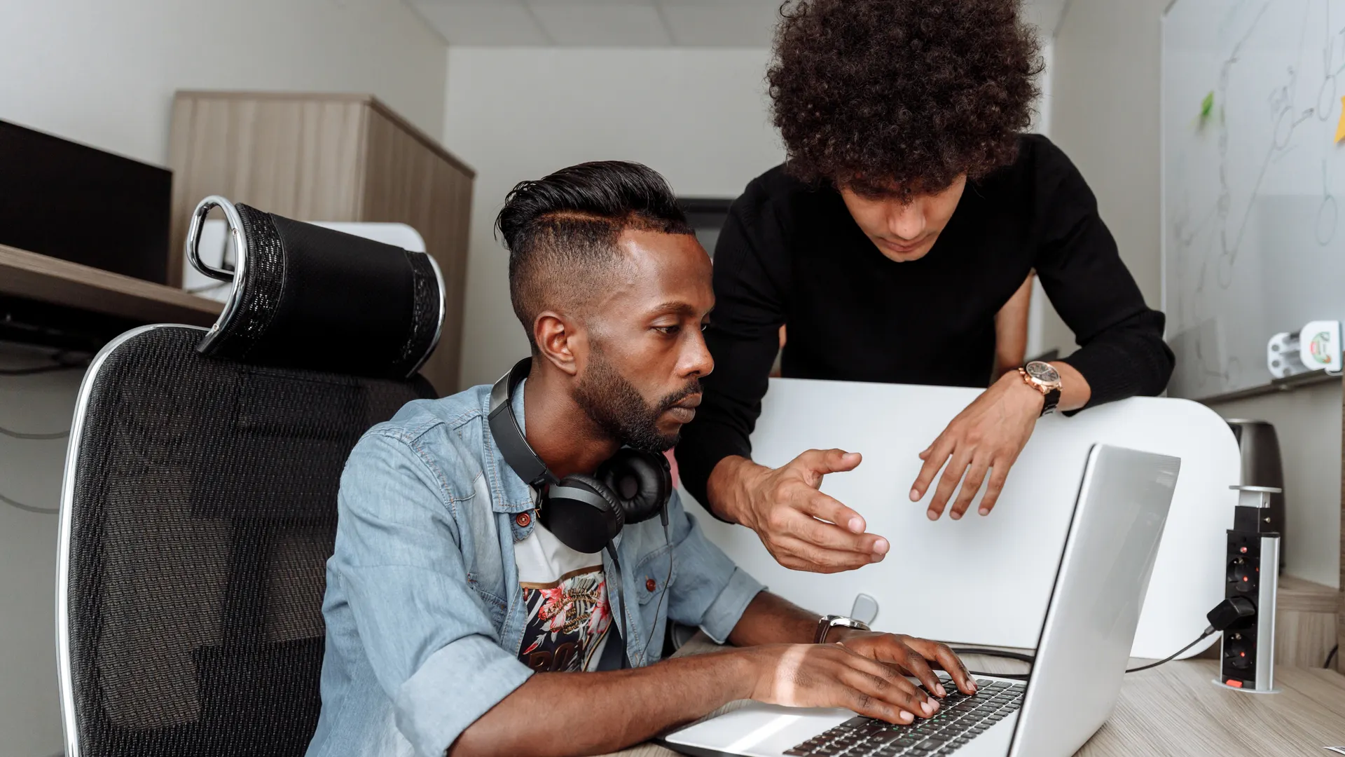 Two diverse male colleagues collaborating on a laptop in a modern office environment