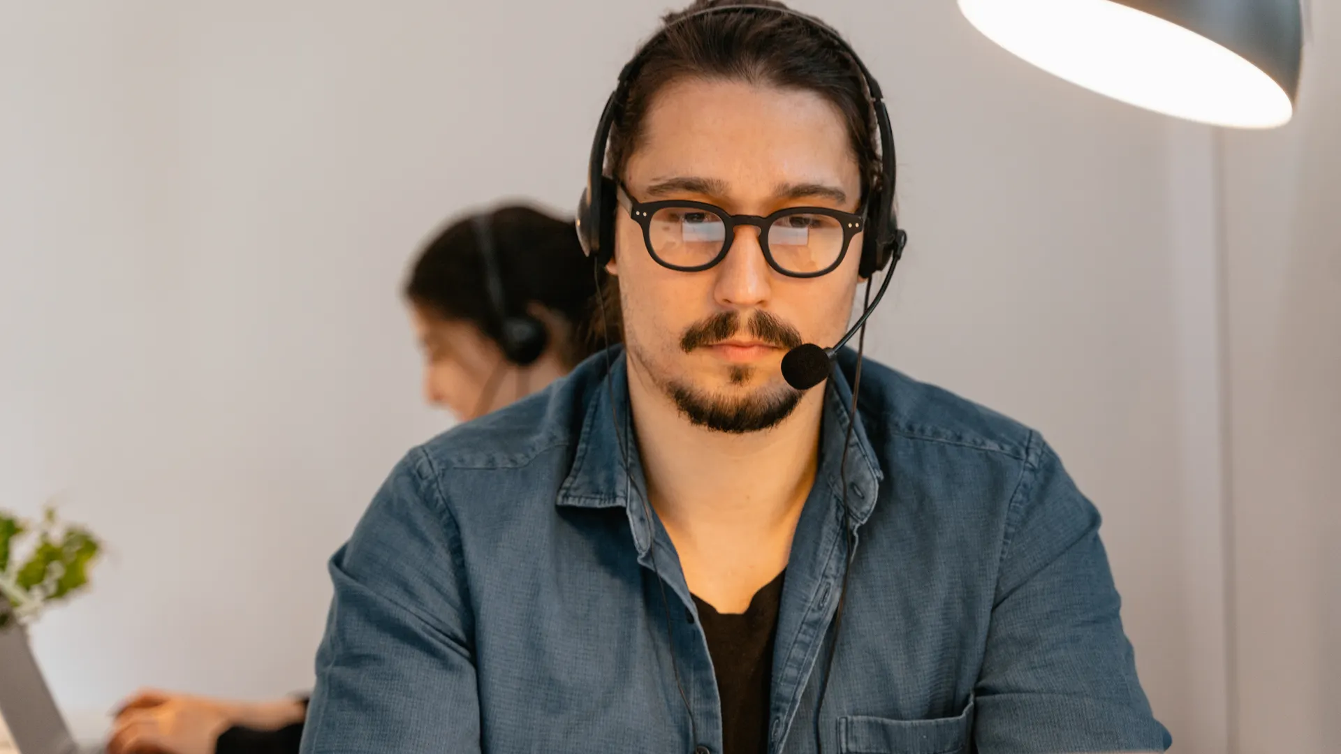A call center agent wearing headphones, working intently at his desk in a modern office environment