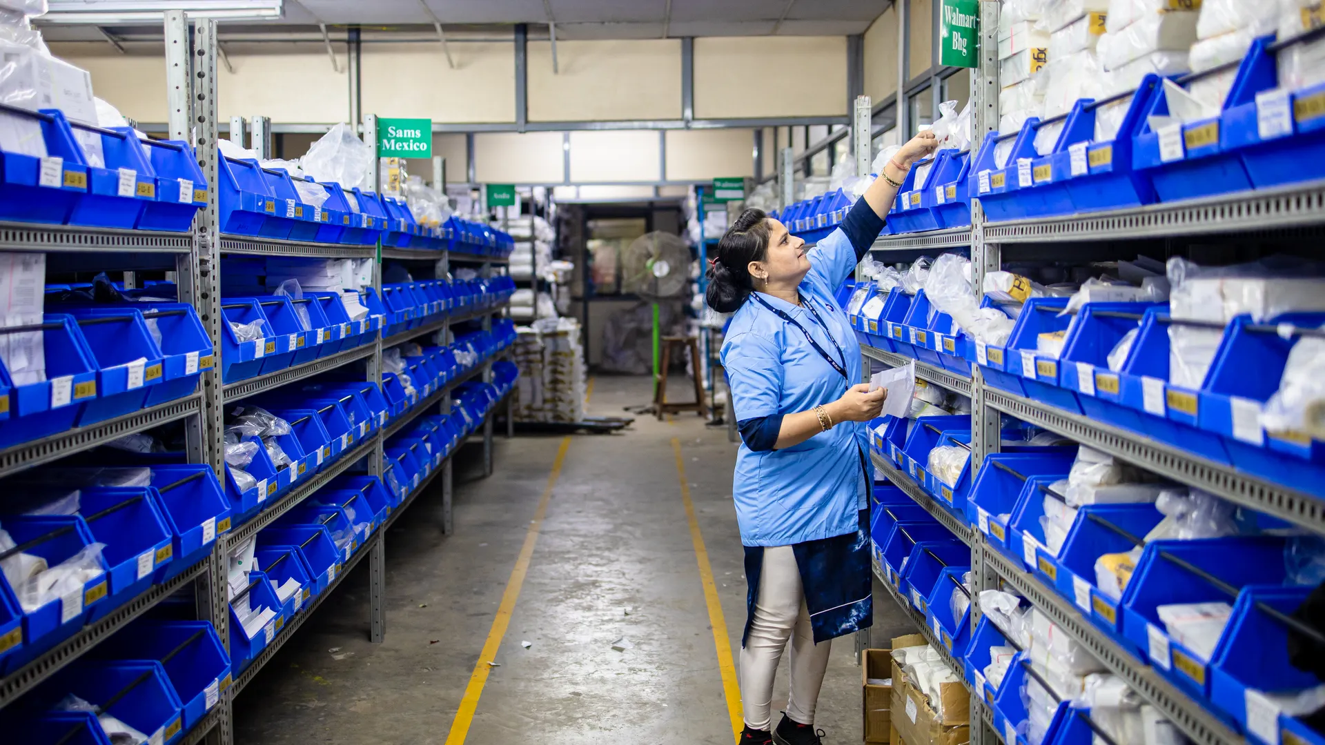 Woman in uniform organizing inventory in a warehouse aisle with labeled bins