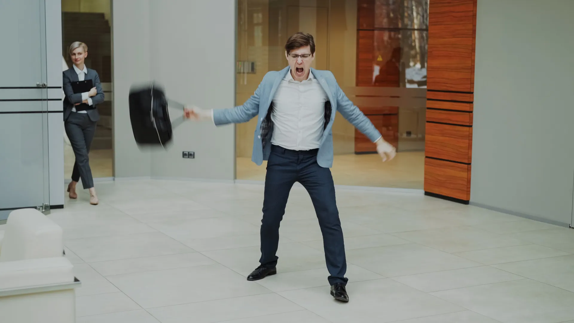A businessman expresses frustration by throwing his briefcase inside a modern office setting