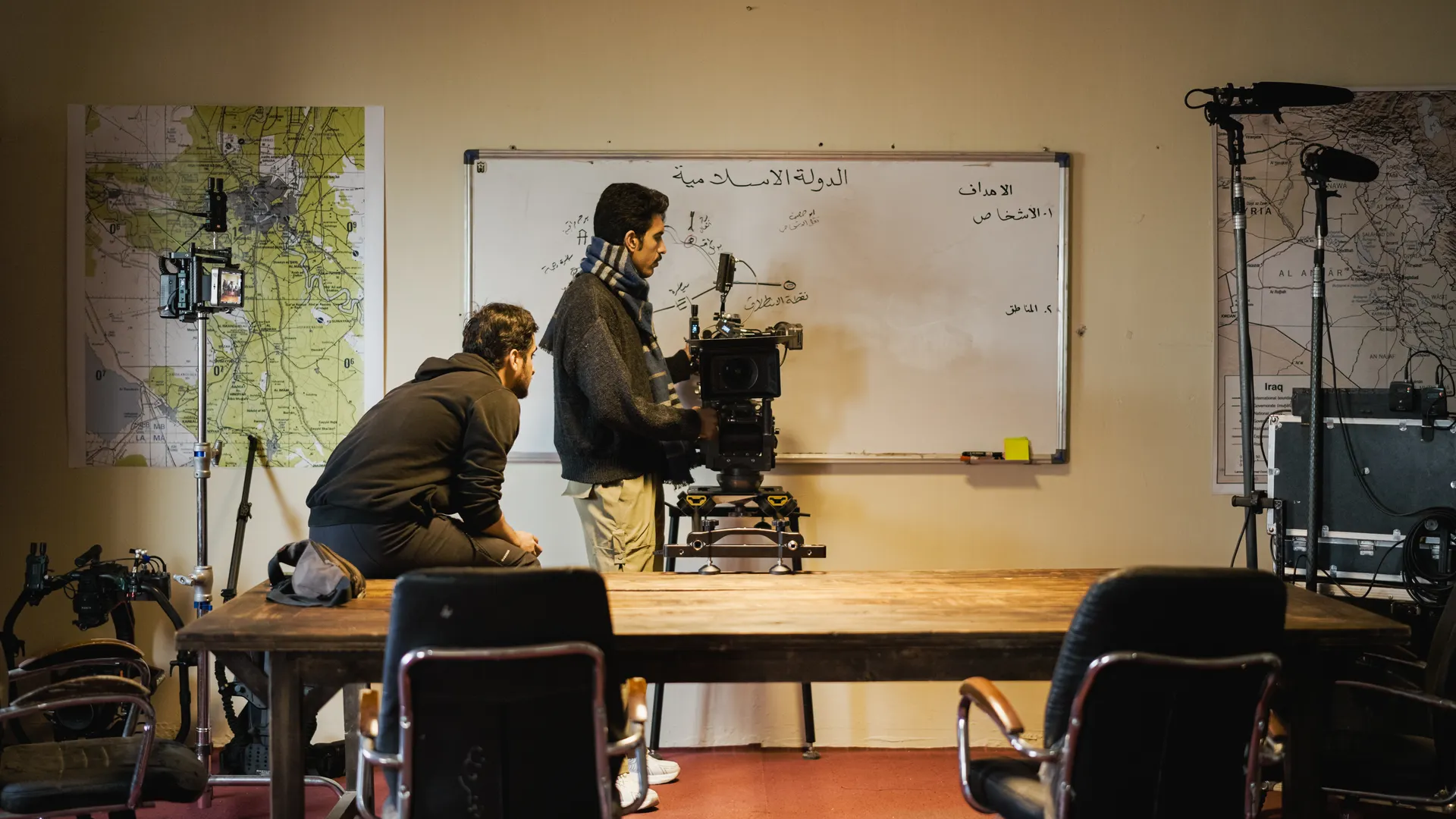Two men setting up a camera in an indoor film studio. Maps and equipment surround them