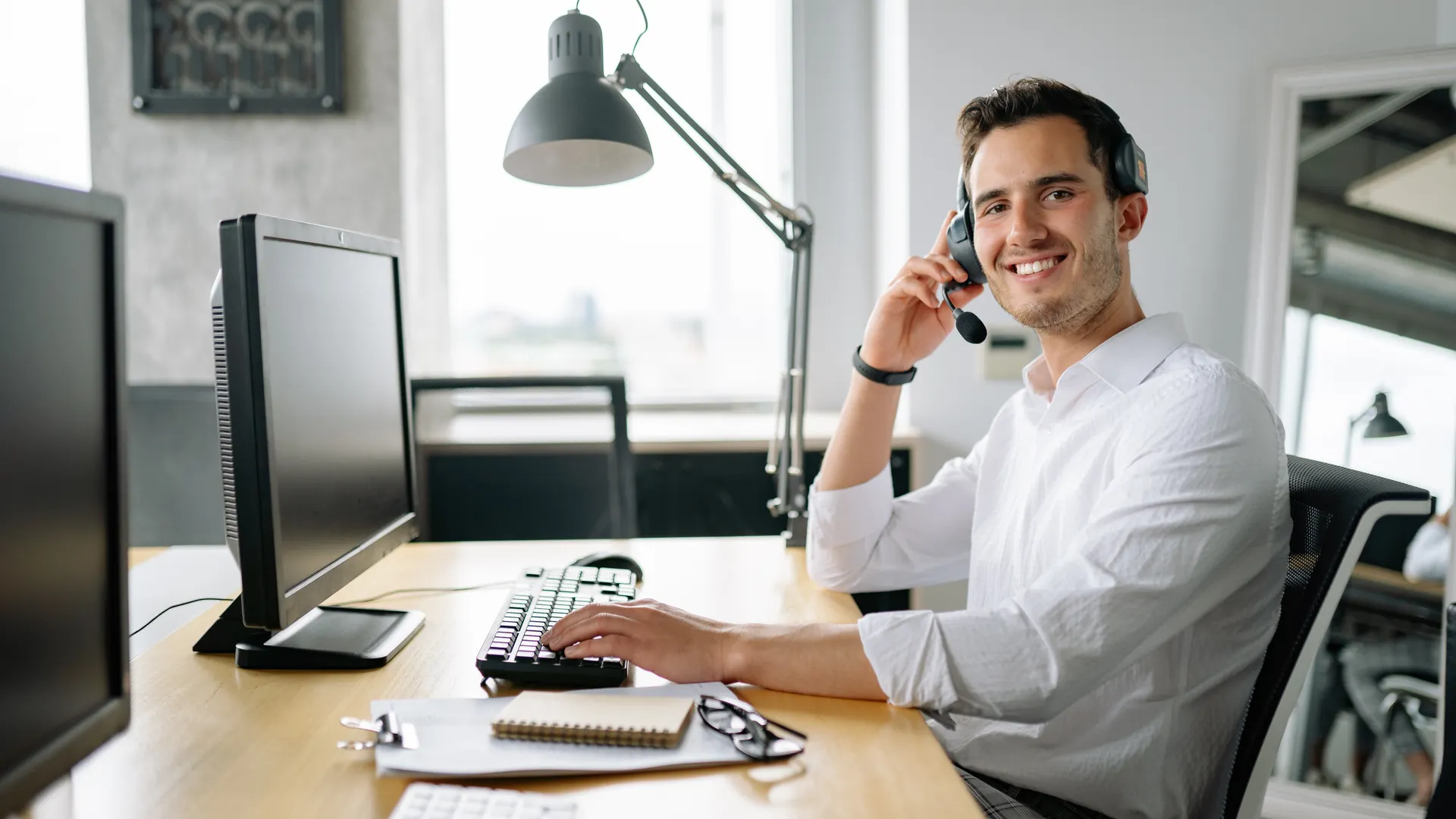 Smiling call center agent working at a desk with a headset and computer in a modern office