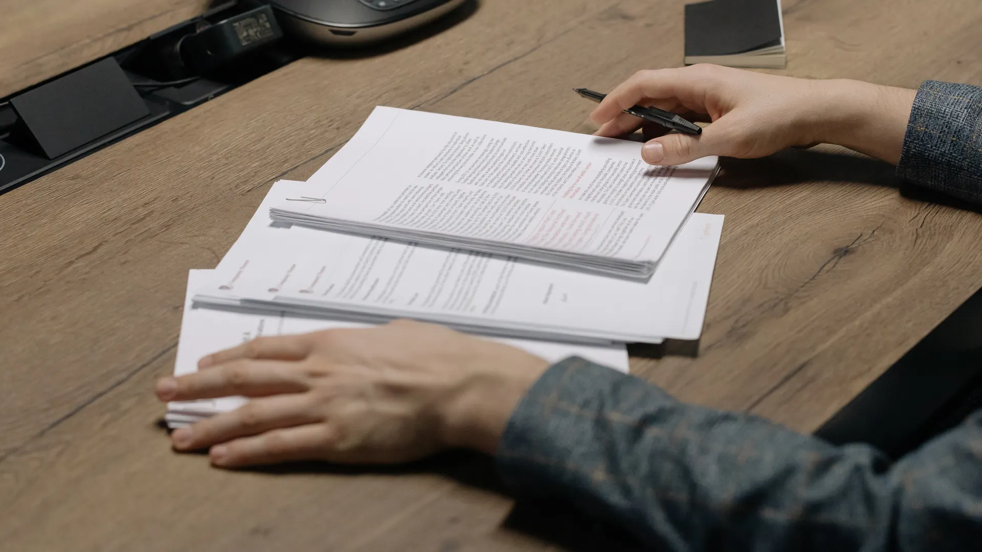 Close-up of a person reviewing documents with a pen at a modern office desk