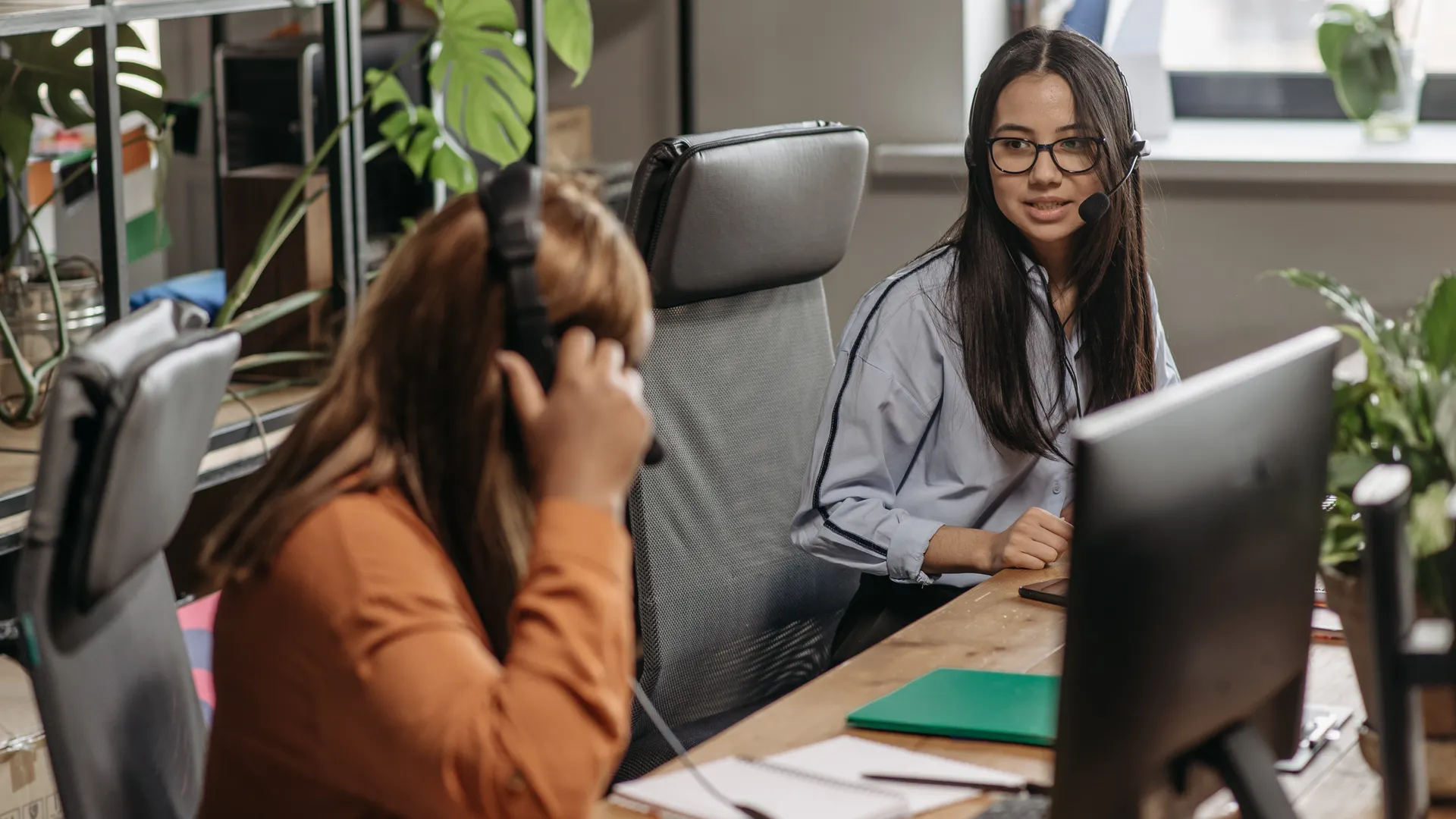 Two women working together in a vibrant office space, wearing headsets and engaging in teamwork