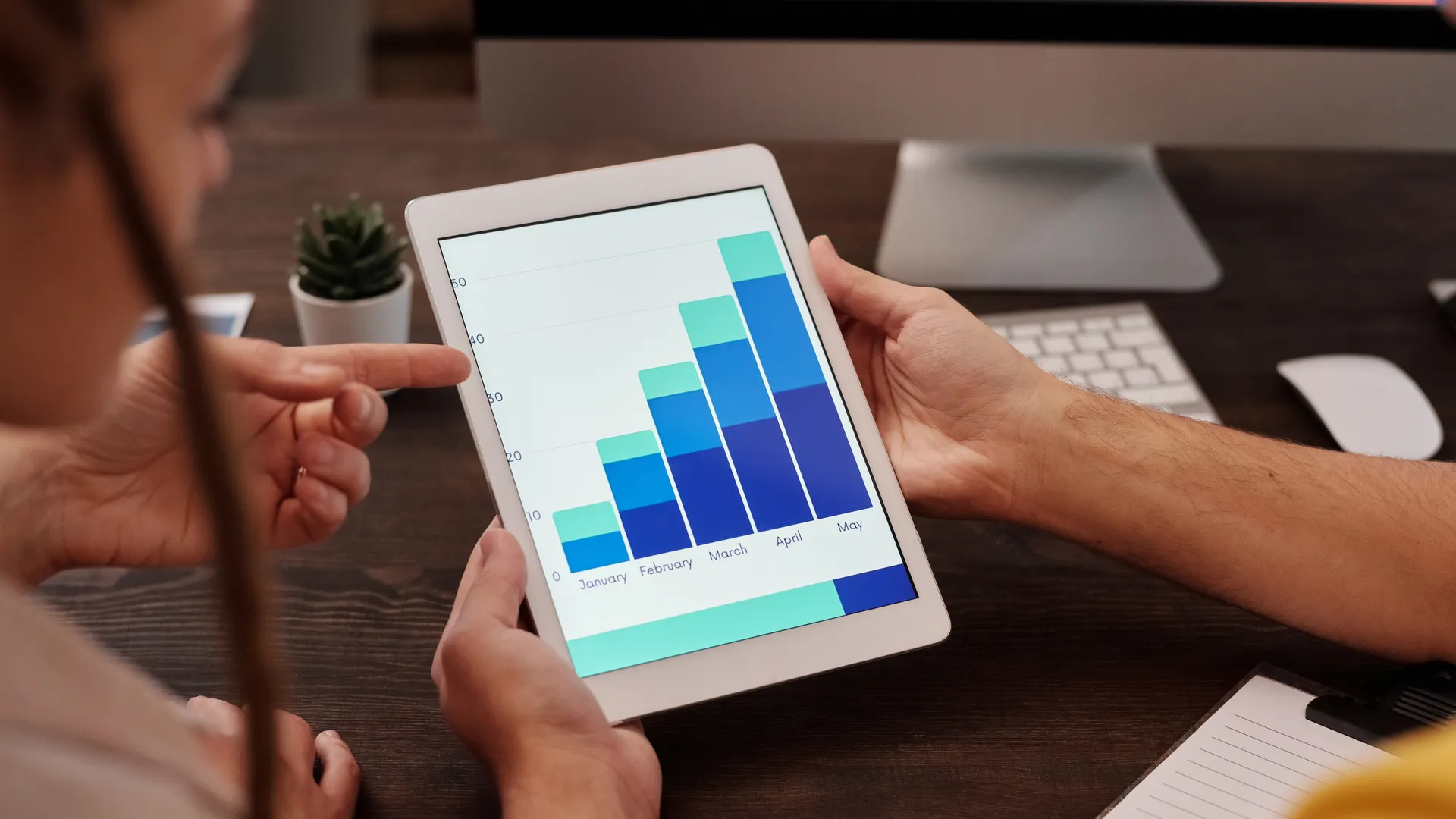 Two adults working in an office, examining graphs on a tablet screen for data analysis