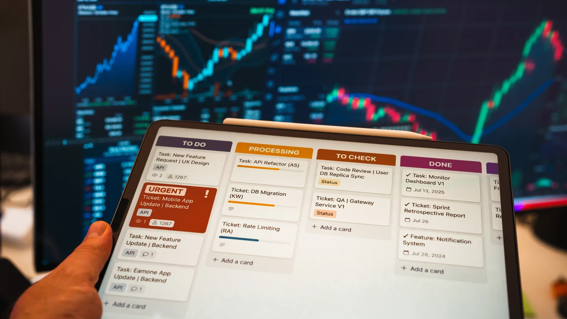 Tablet with business task management app in front of stock chart monitors