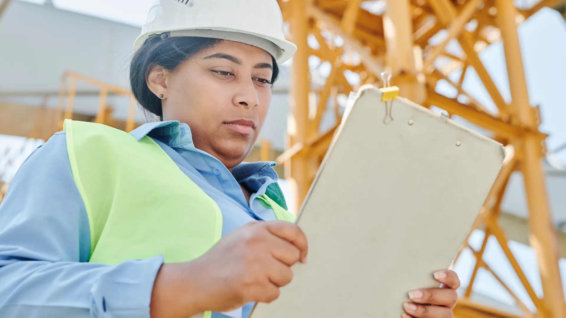 Confident female construction worker inspecting site with clipboard and helmet