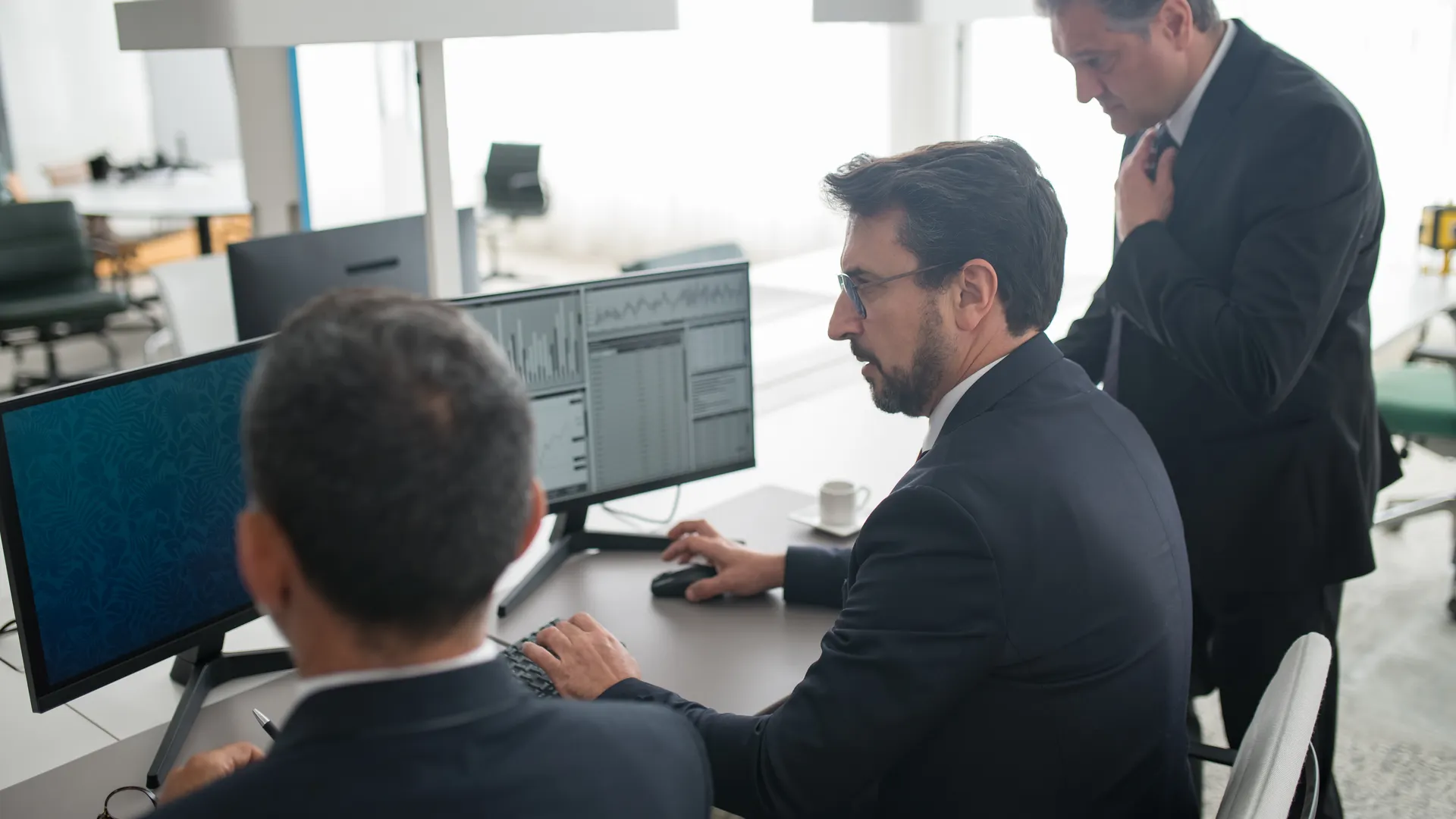 Colleagues in a modern office reviewing stock market trends and data on multiple screens