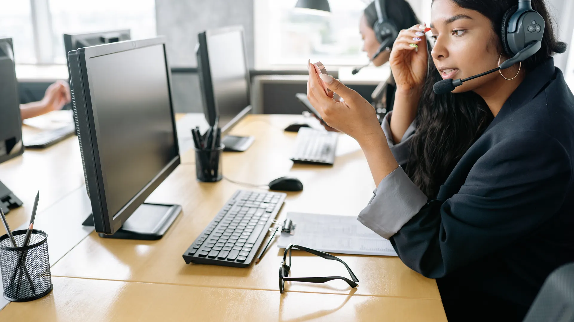 South Asian woman providing customer support in a modern office environment, equipped with a headset