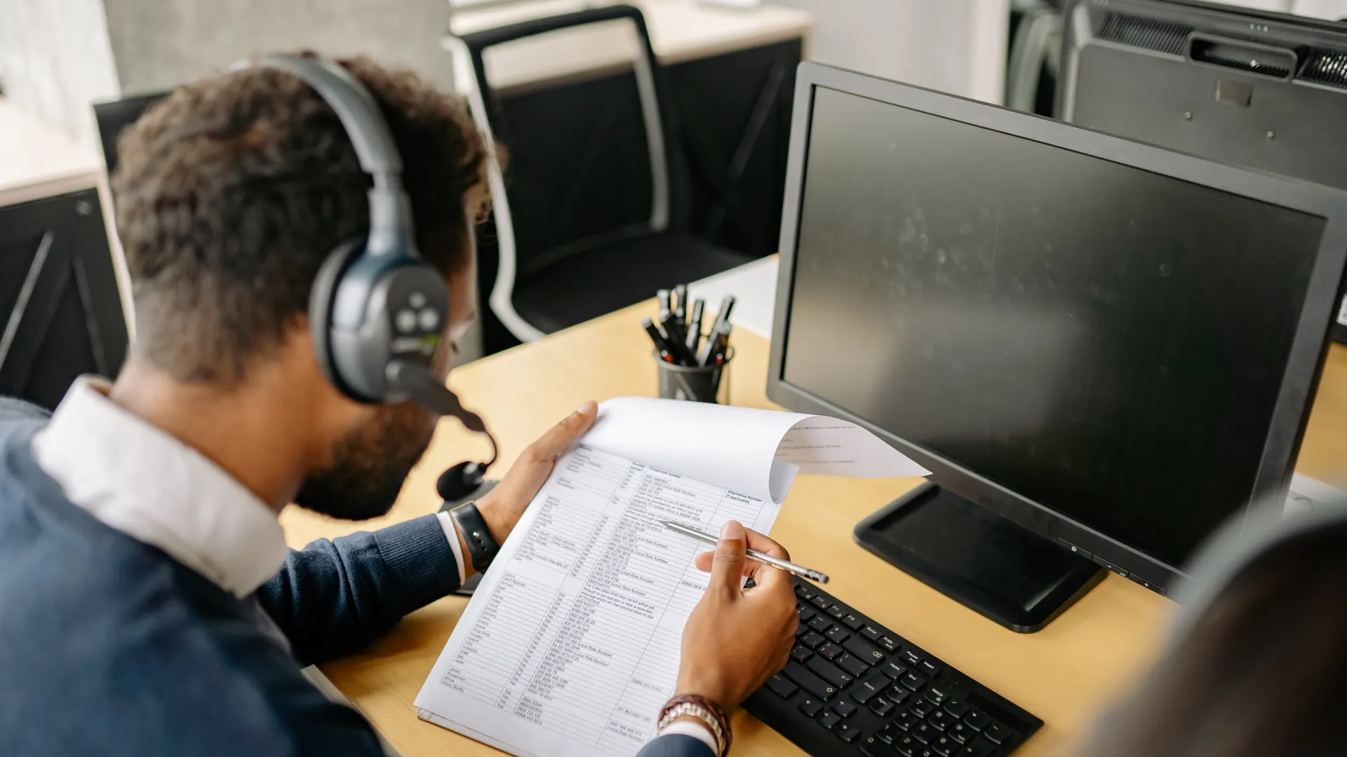 Adult male using a computer and headset, reviewing documents in a modern office setting