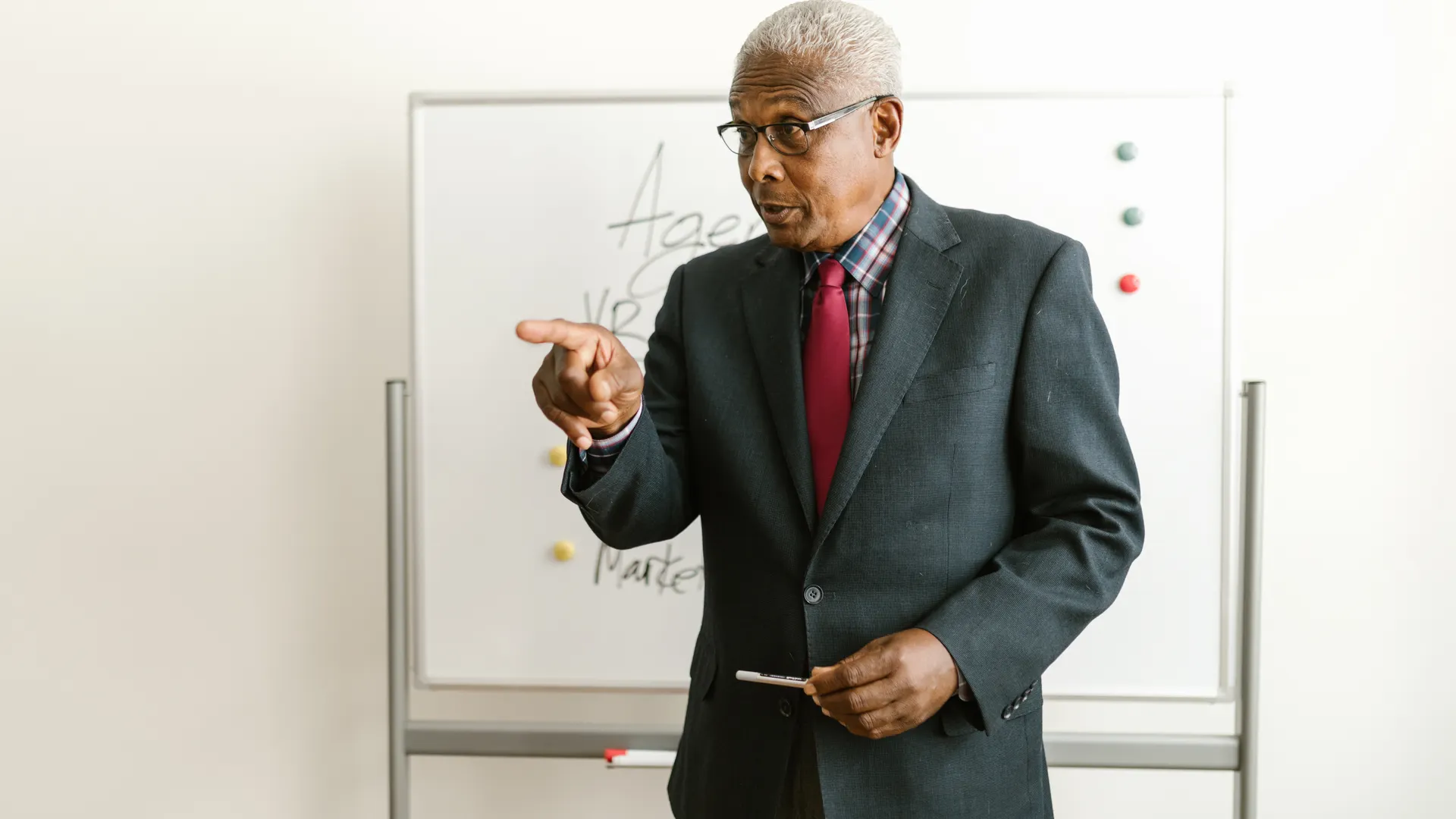 Elderly man in business attire giving a presentation in front of a whiteboard