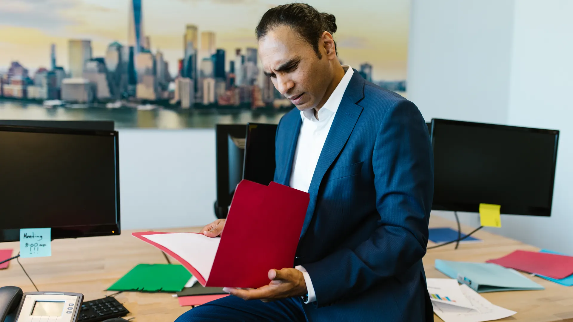 Businessman in an office reviewing documents with a serious expression, surrounded by computers and