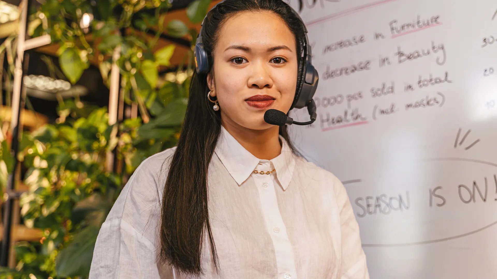 Confident woman wearing a headset in a modern office setting with a whiteboard