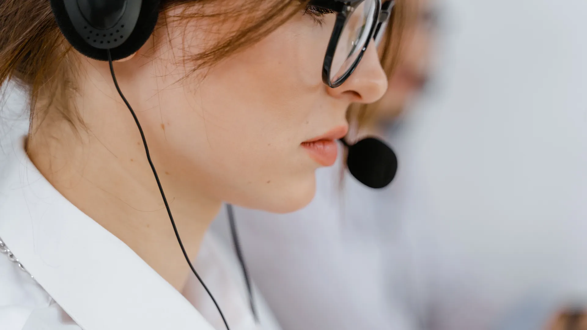 A young woman with glasses and headset intensely focused on her work in an office environment