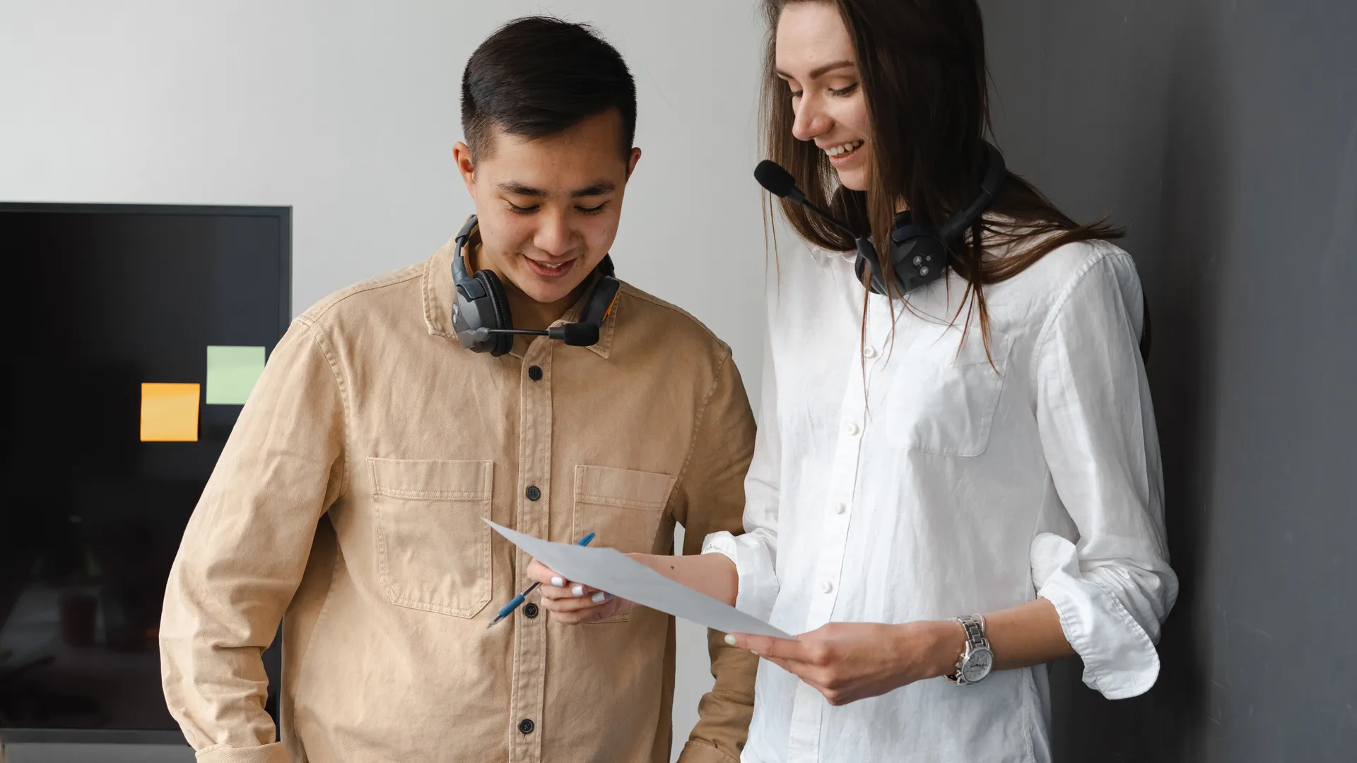 Two colleagues discussing a document in an office setting, wearing headsets