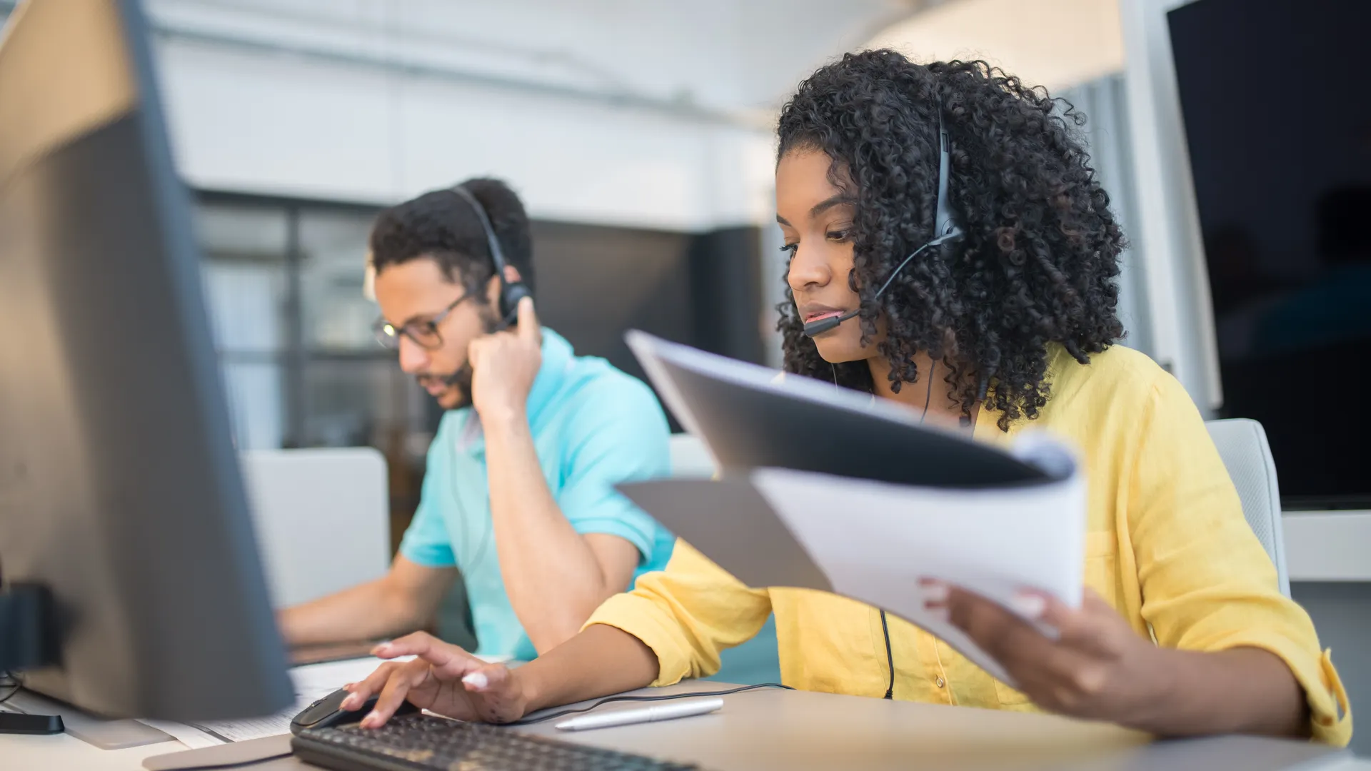Two customer service representatives working with headsets in a modern office setting