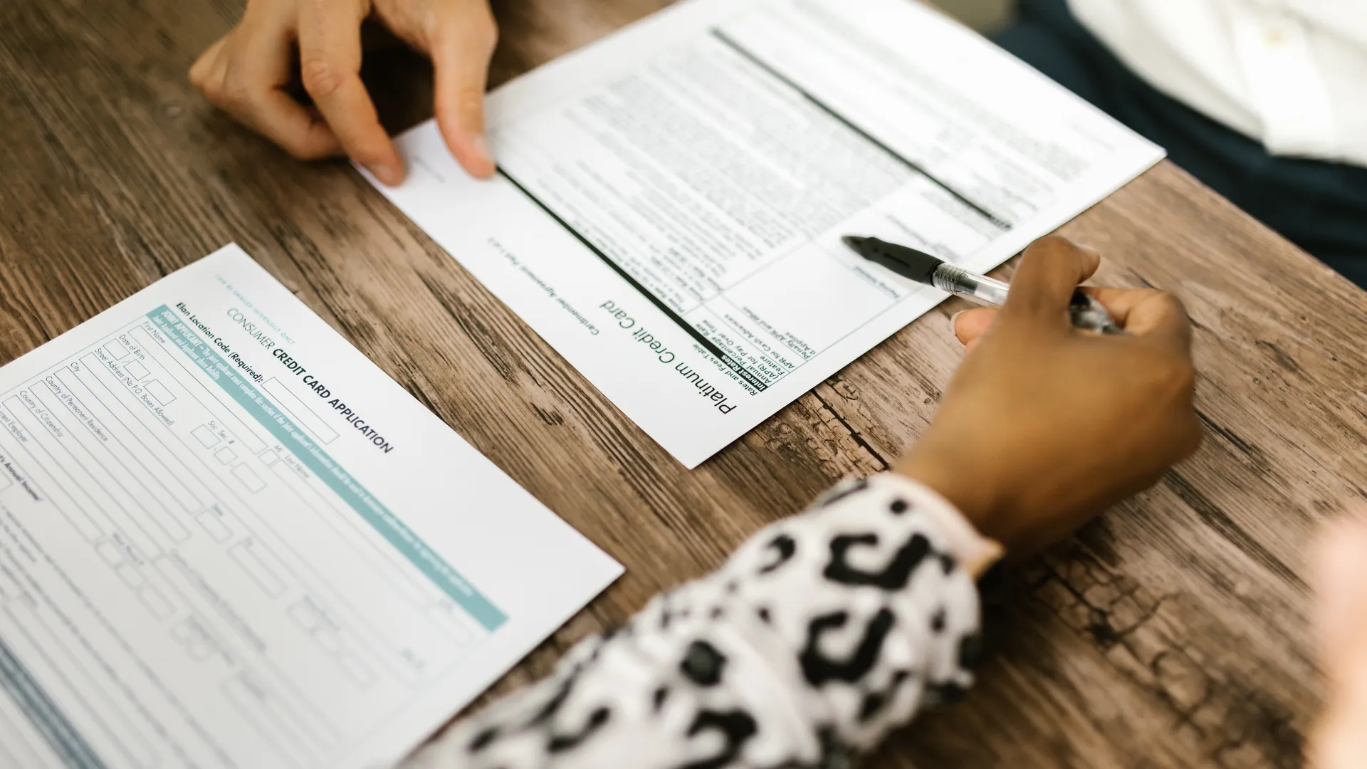 Close-up of two people reviewing and filling out a credit card application on a wooden table