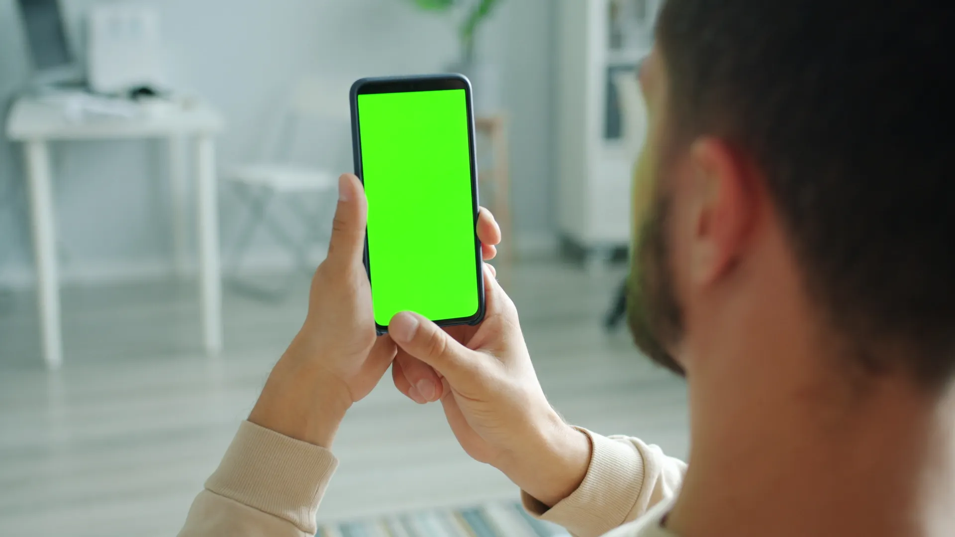 Man holding smartphone with green screen for mockup application indoors