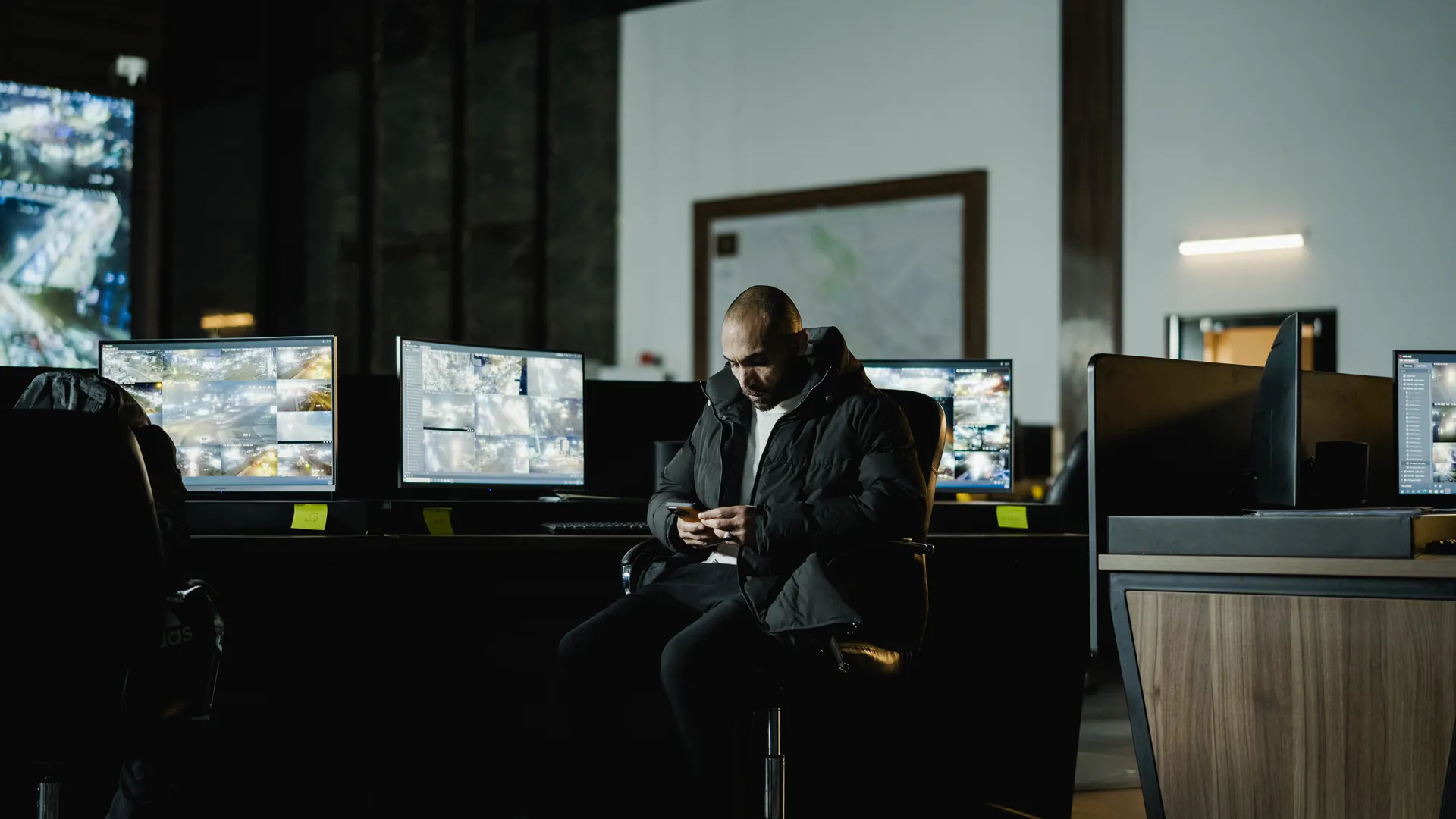 Security officer seated in a dimly lit control room, analyzing multiple surveillance screens