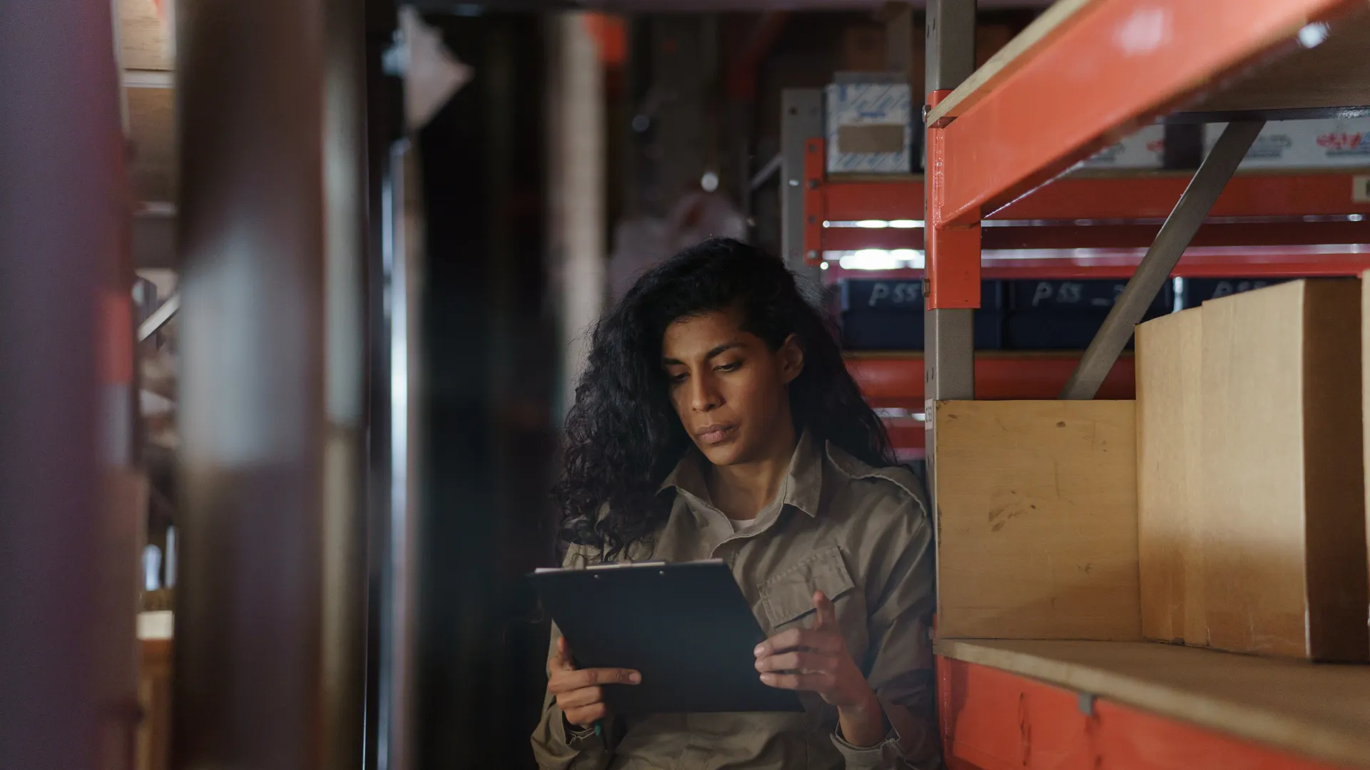 Woman in warehouse taking inventory with clipboard, focused and pensive