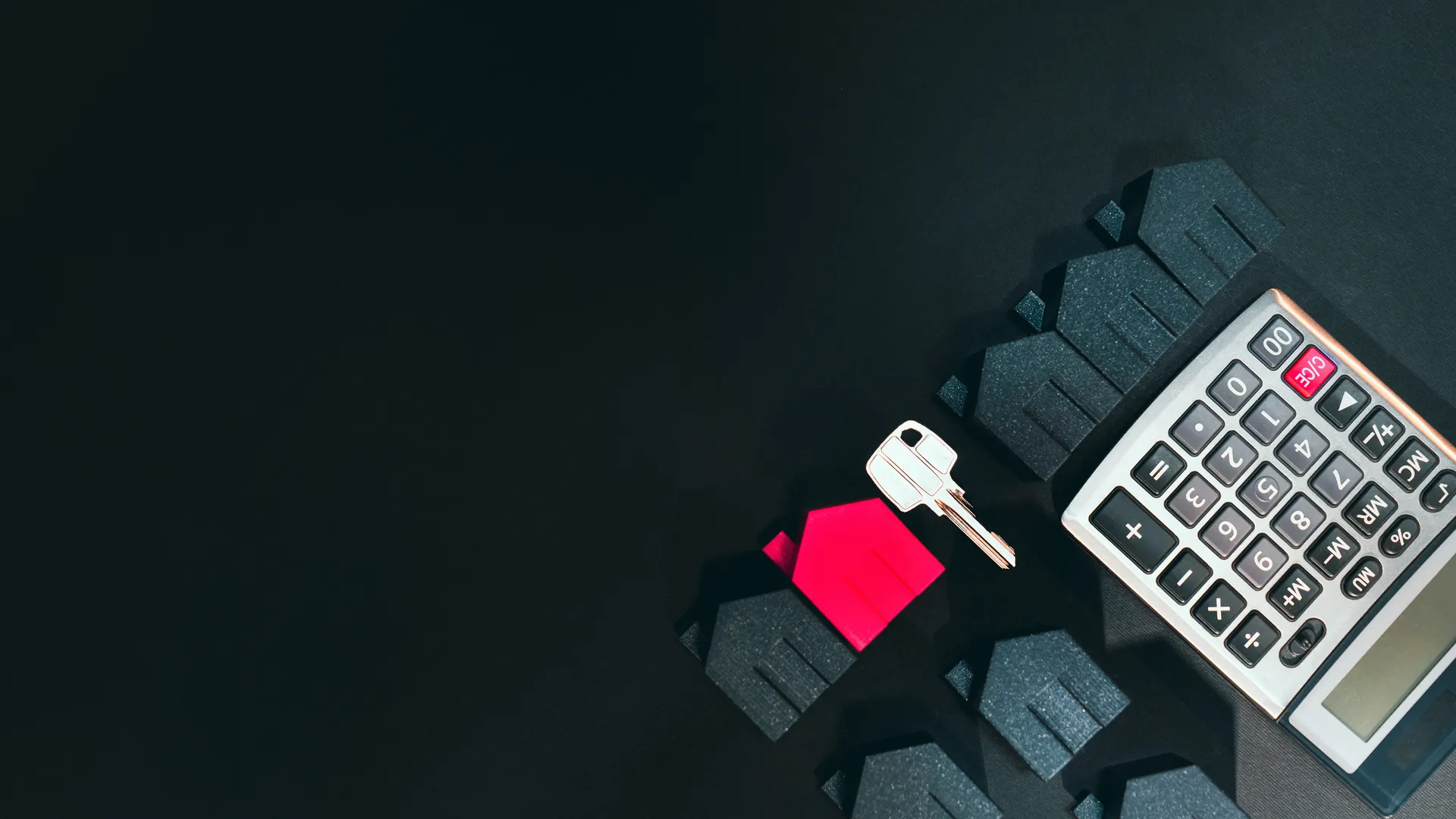 Real estate concept image featuring a calculator, houses, and a key on a black background