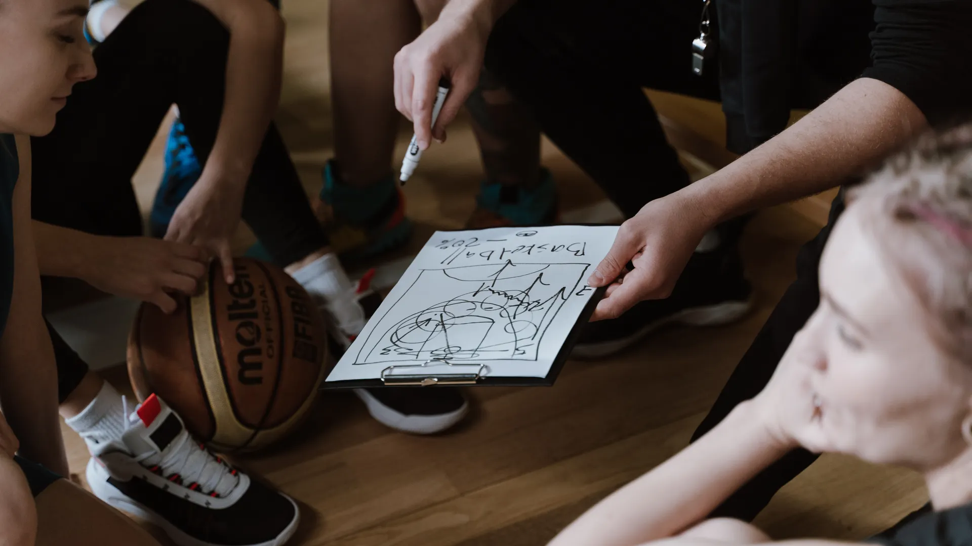 Close-up of a basketball team huddling with the coach discussing strategy indoors