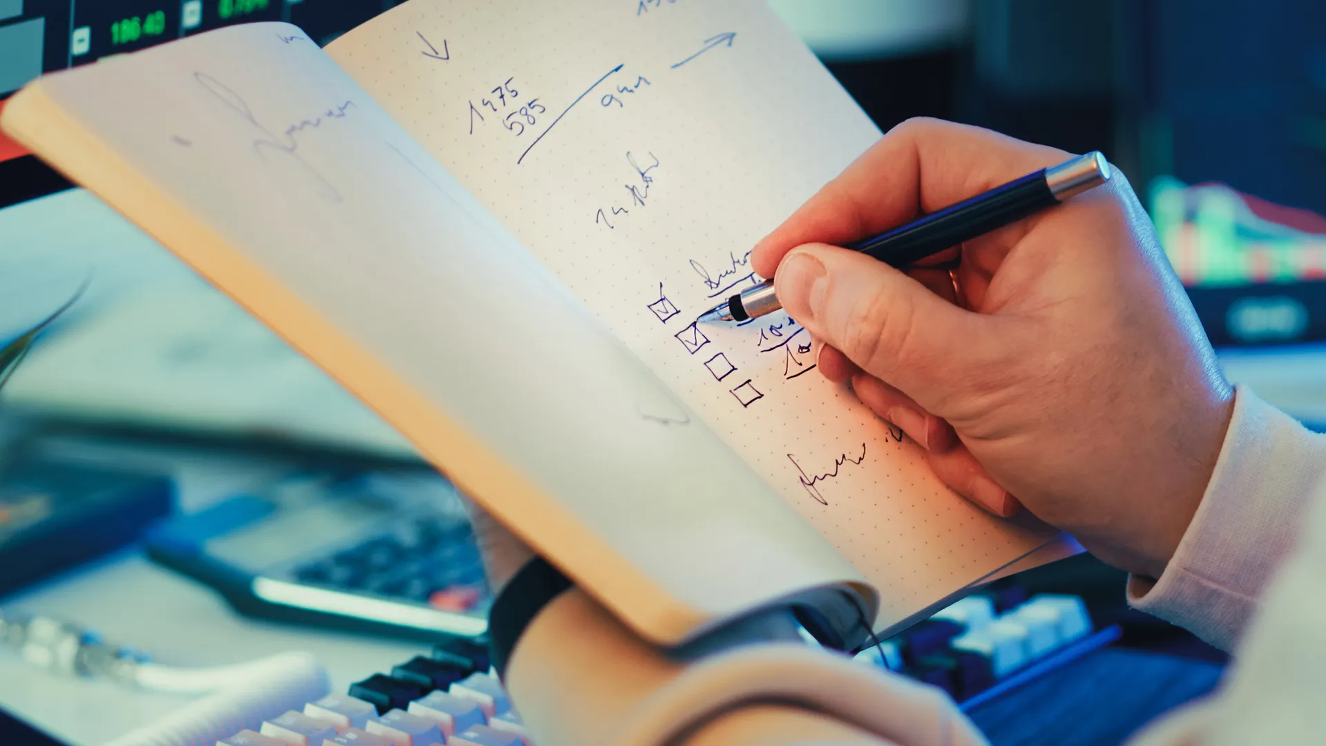A hand writing in a notebook during stock market analysis on a desk