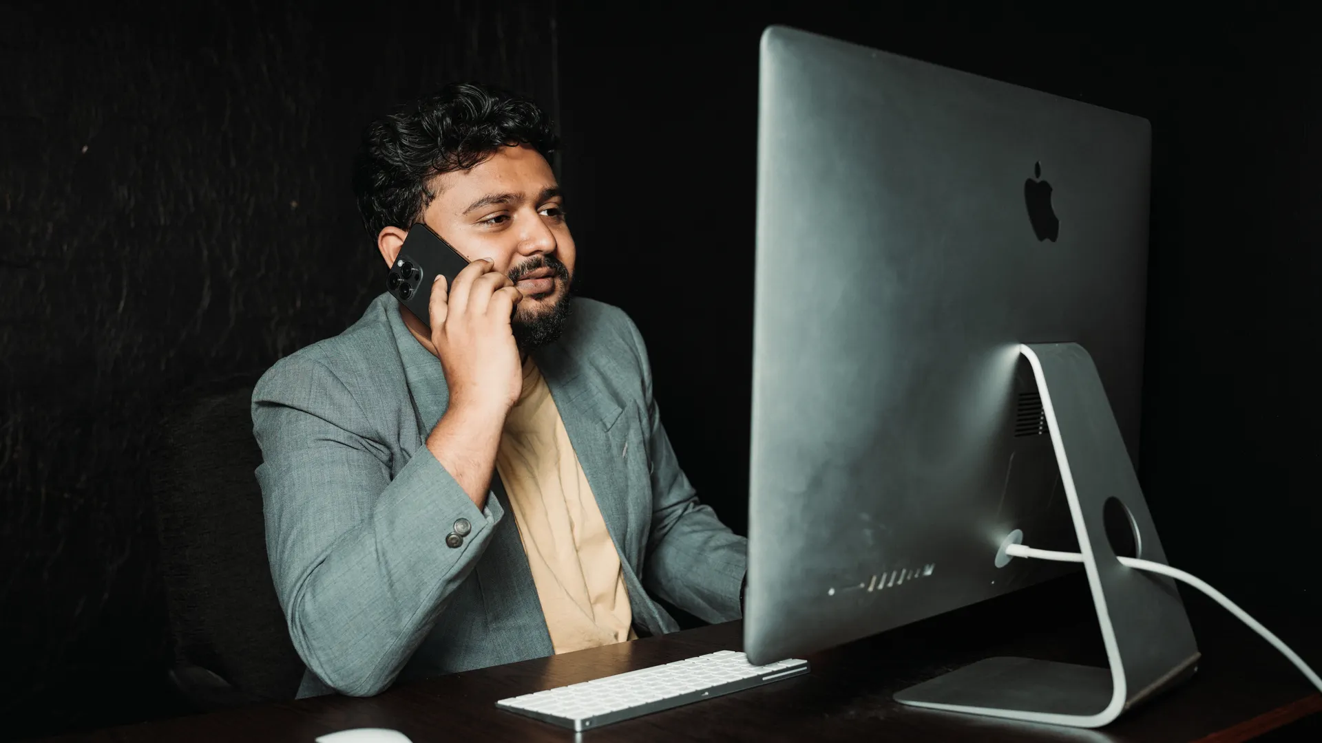 Professional man multitasking at office desk using computer and smartphone