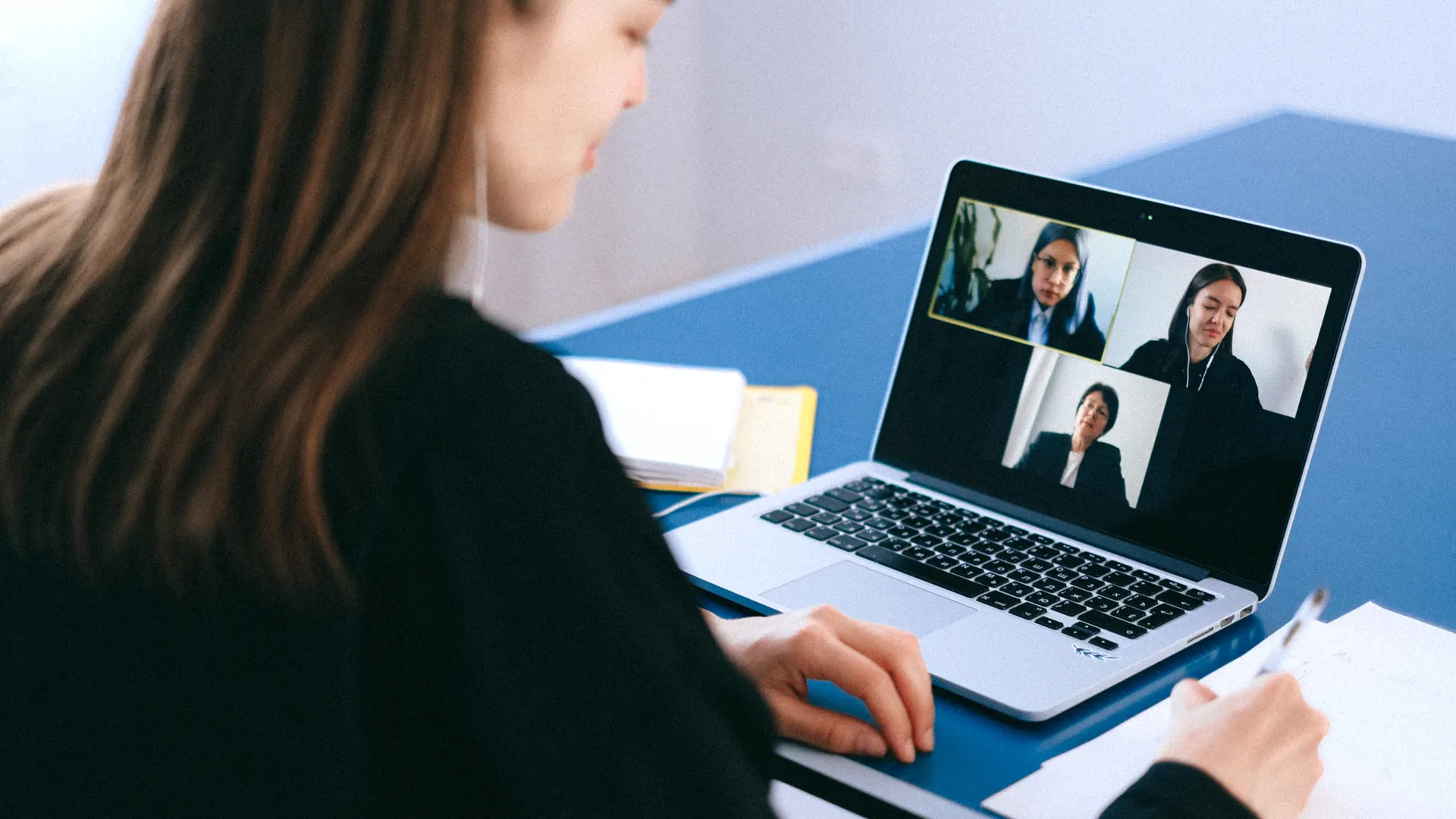 A woman engaging in a video conference using a laptop at home, taking notes