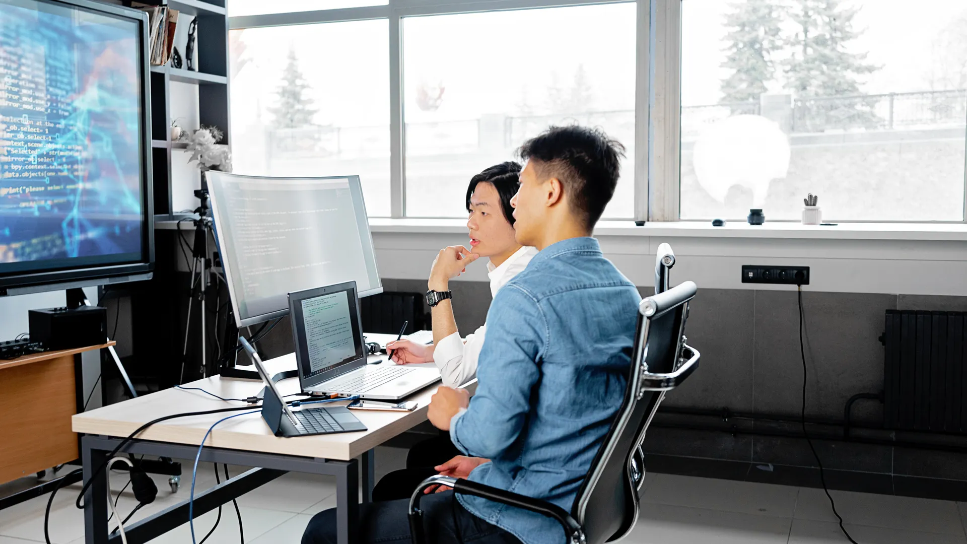 Two men analyzing code on computers in a modern office setting