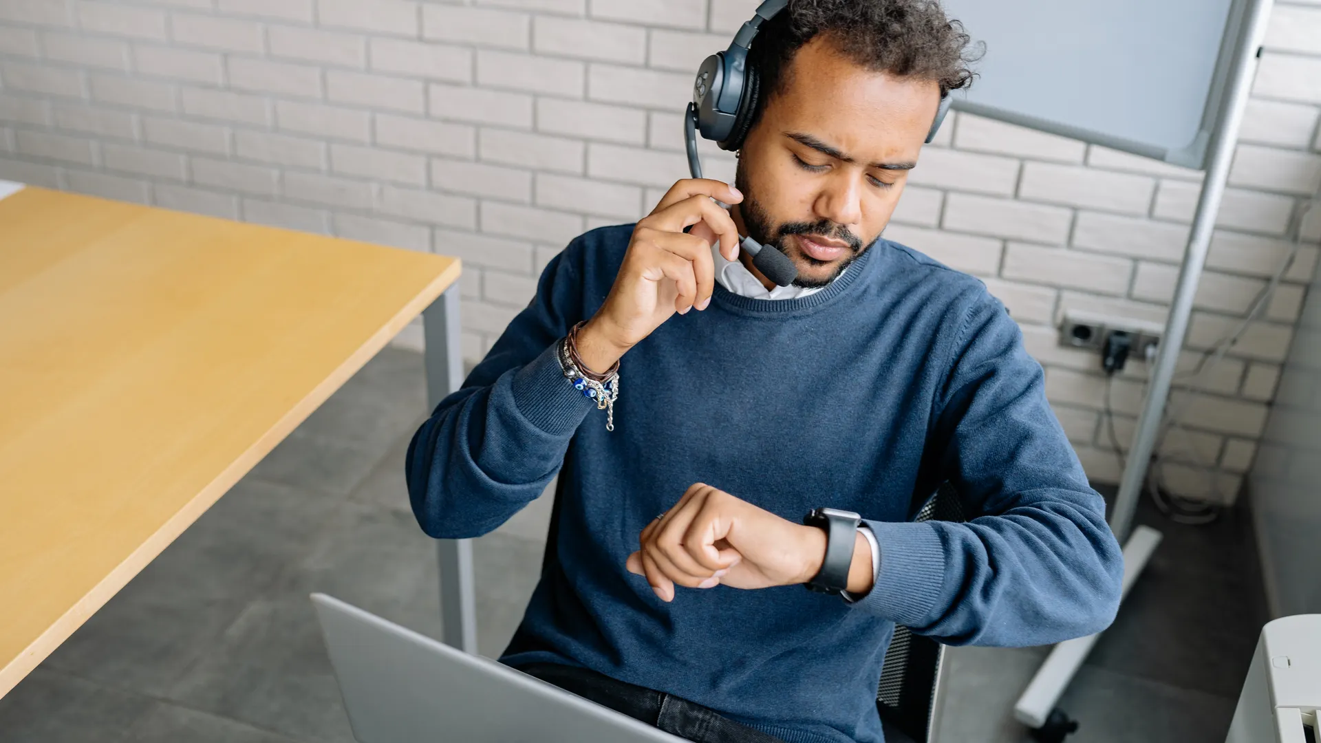 A focused call center agent wearing a headset checks the time on his wristwatch