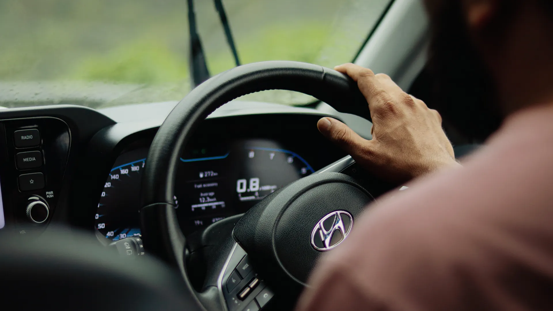 Photo of a person driving a Hyundai car in rainy weather, focus on steering wheel