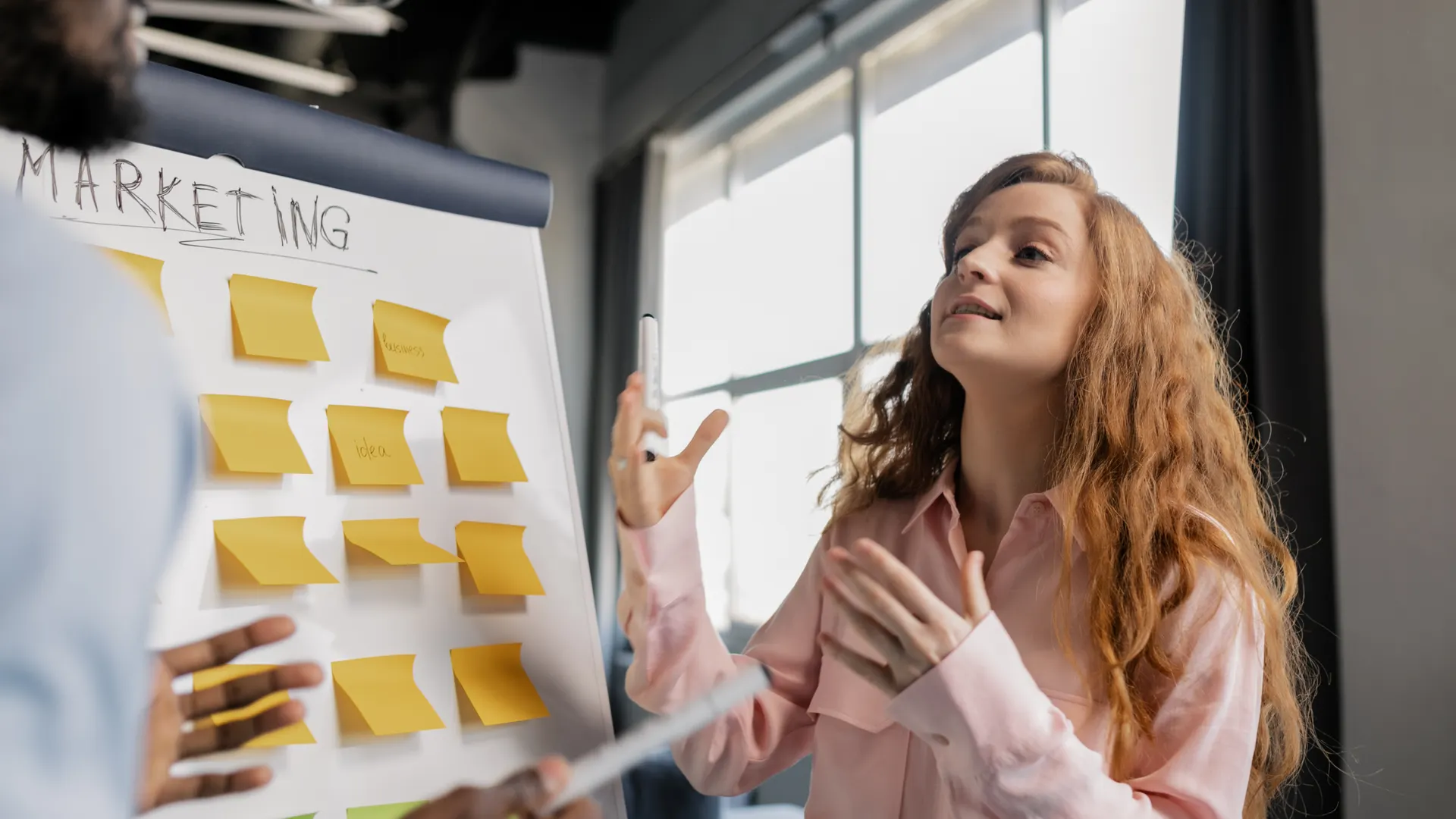Woman in a business meeting discussing marketing strategies using sticky notes on a board