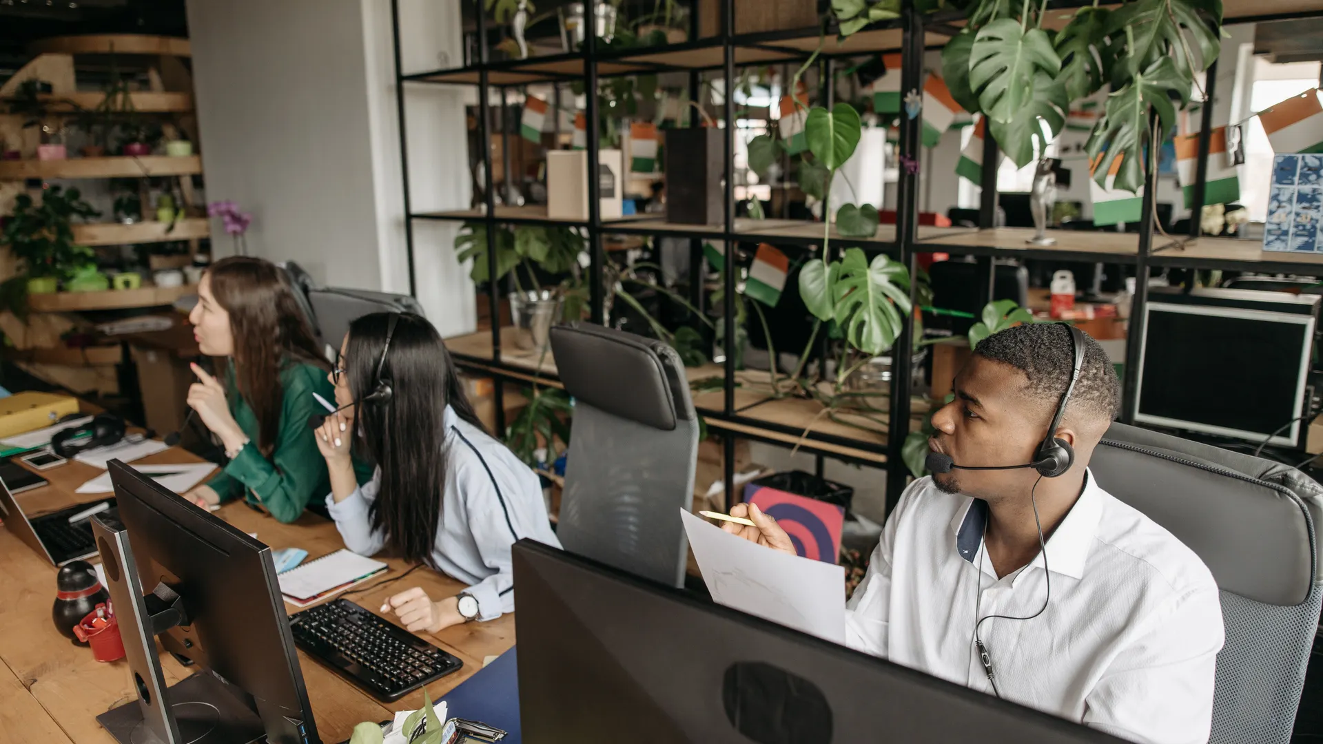 A diverse team collaborates in a modern office with plants and technology