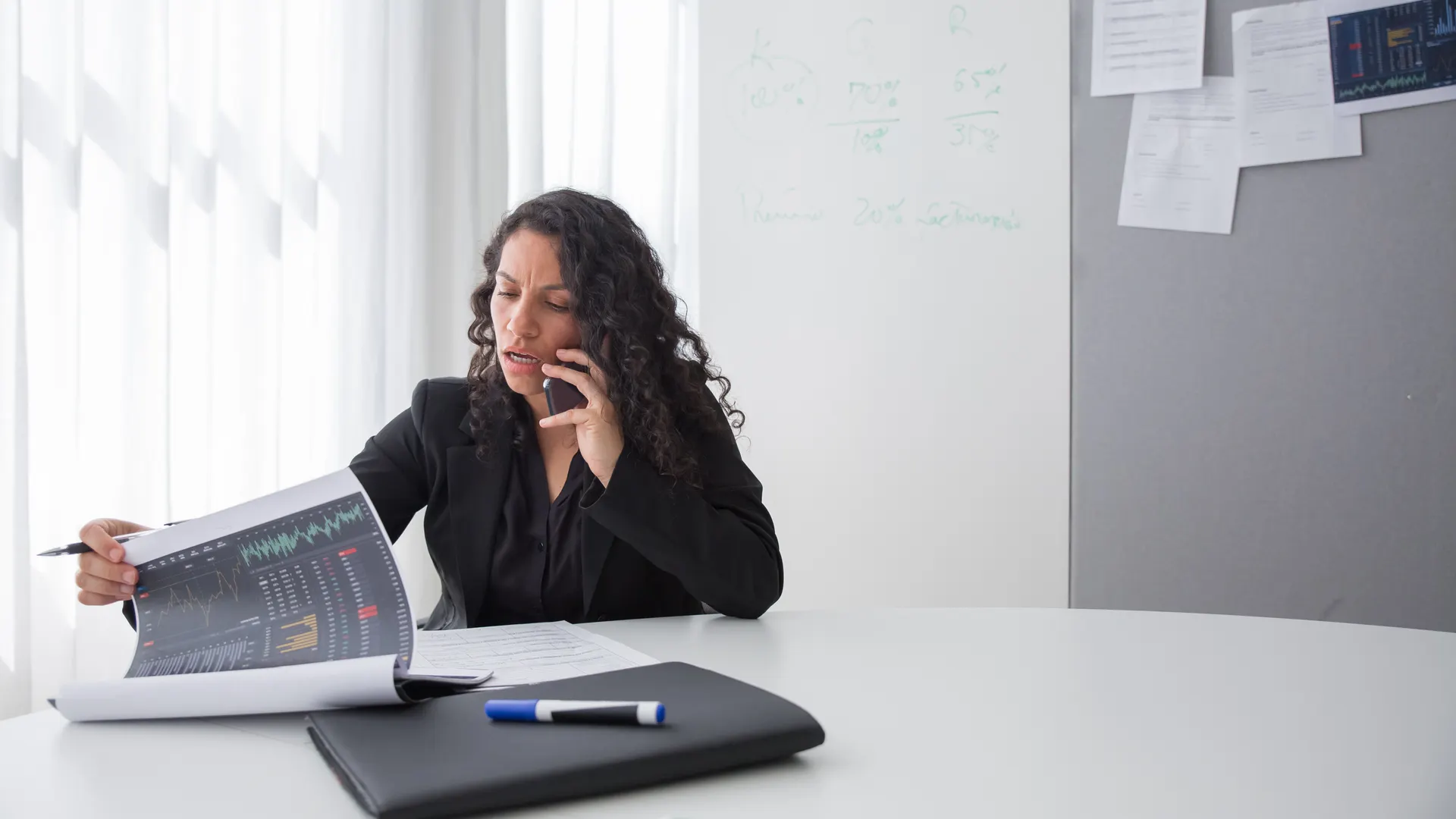 Focused businesswoman reviewing data charts during a phone call in a modern office setting