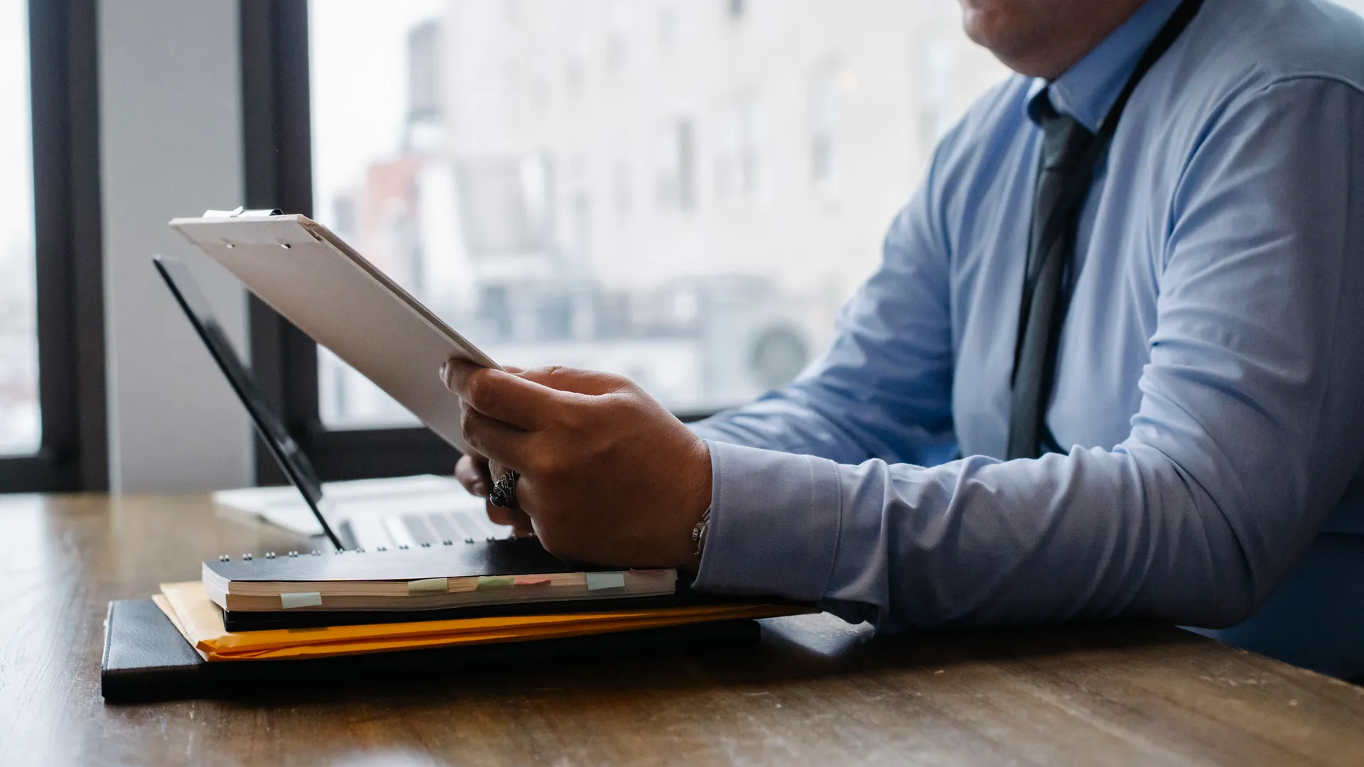 Crop unrecognizable male manager wearing blue shirt and black tie sitting at wooden desk and reading